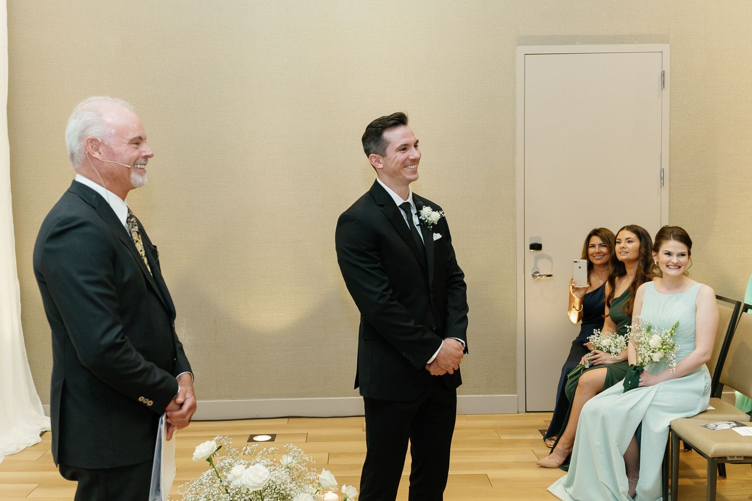 A group of wedding guests and wedding party members gather in a formal event space for photos.