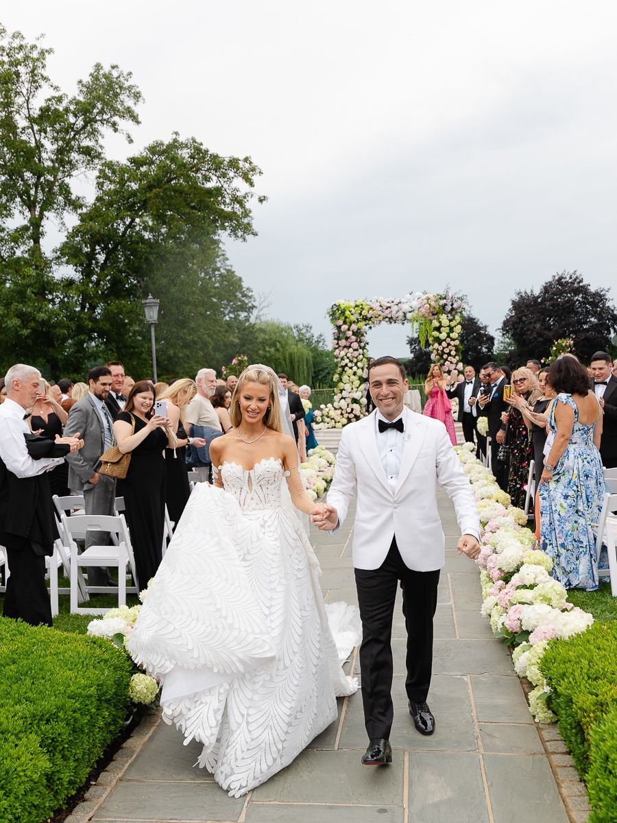 A couple walks down a flower-lined aisle as wedding guests celebrate their joyful outdoor ceremony exit.