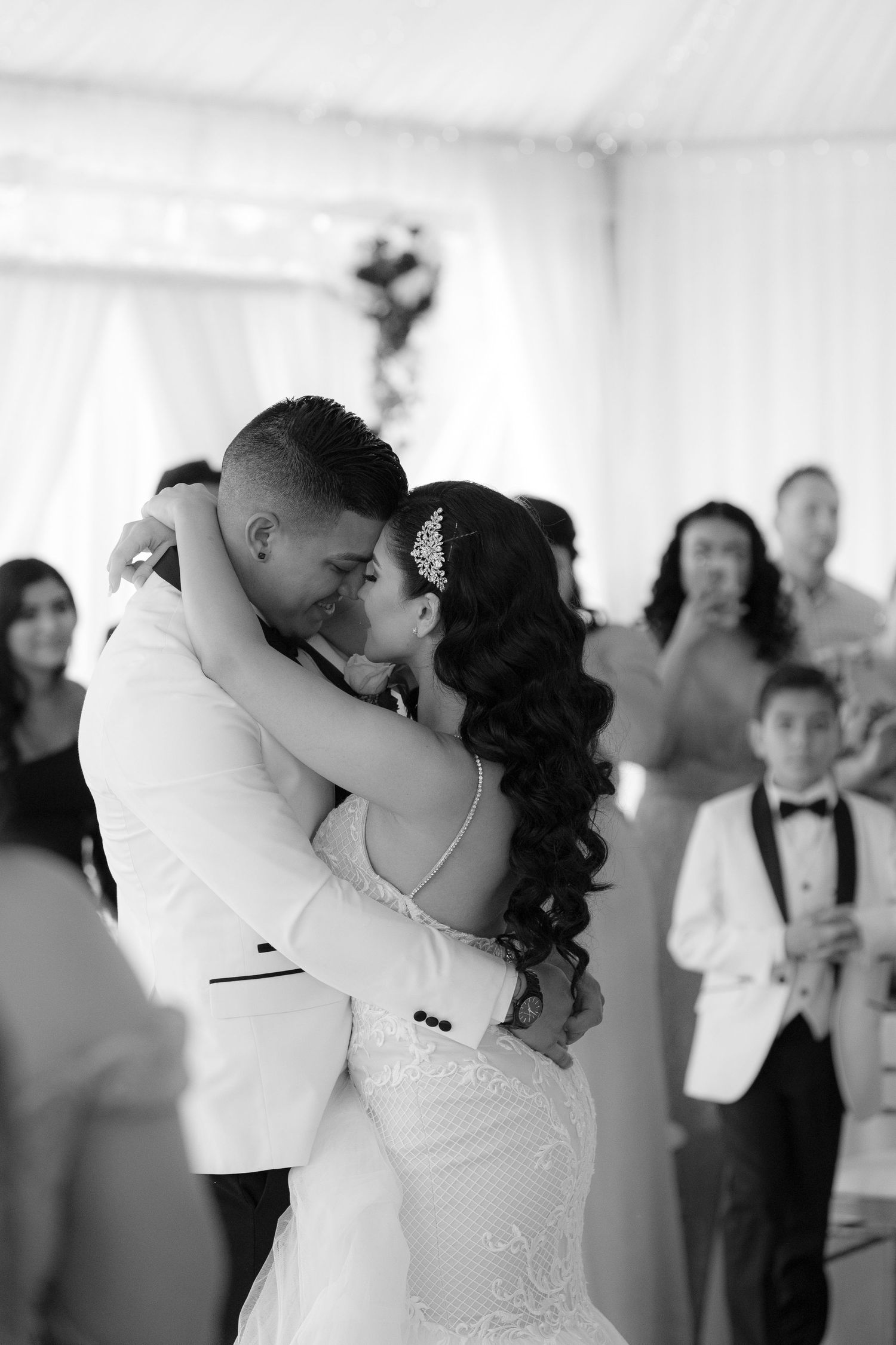 A romantic first dance between newlyweds in white attire as wedding guests look on in a bright reception venue.