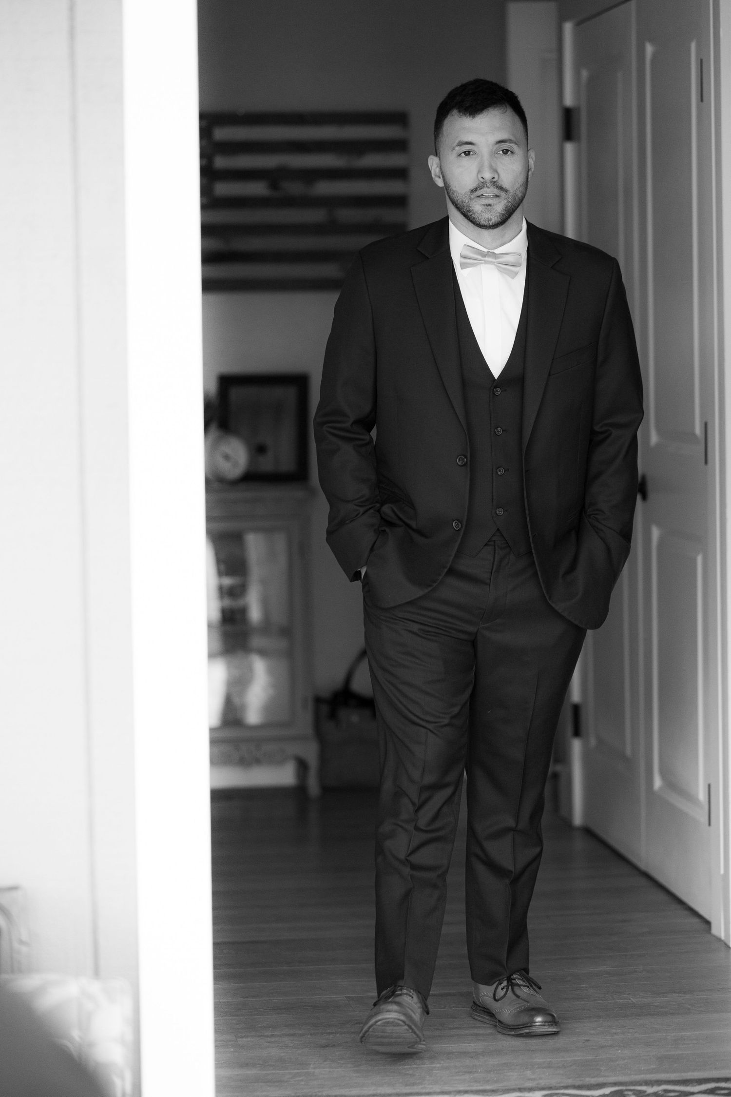 A black and white photograph shows a person in a dark suit standing in a hallway with dramatic lighting.