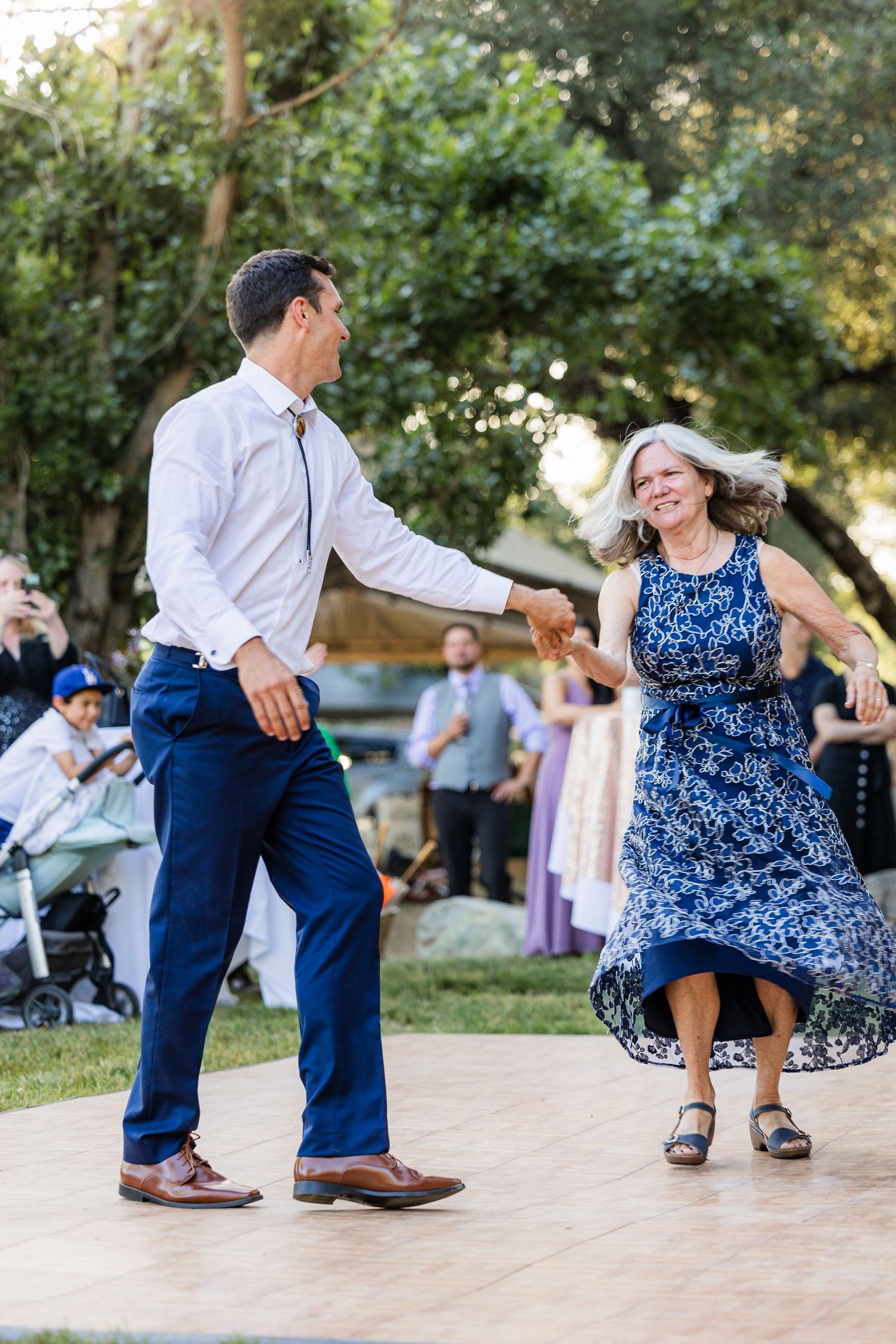 A couple dancing together at an outdoor event, with the woman wearing a blue floral dress and man in white shirt and jeans.