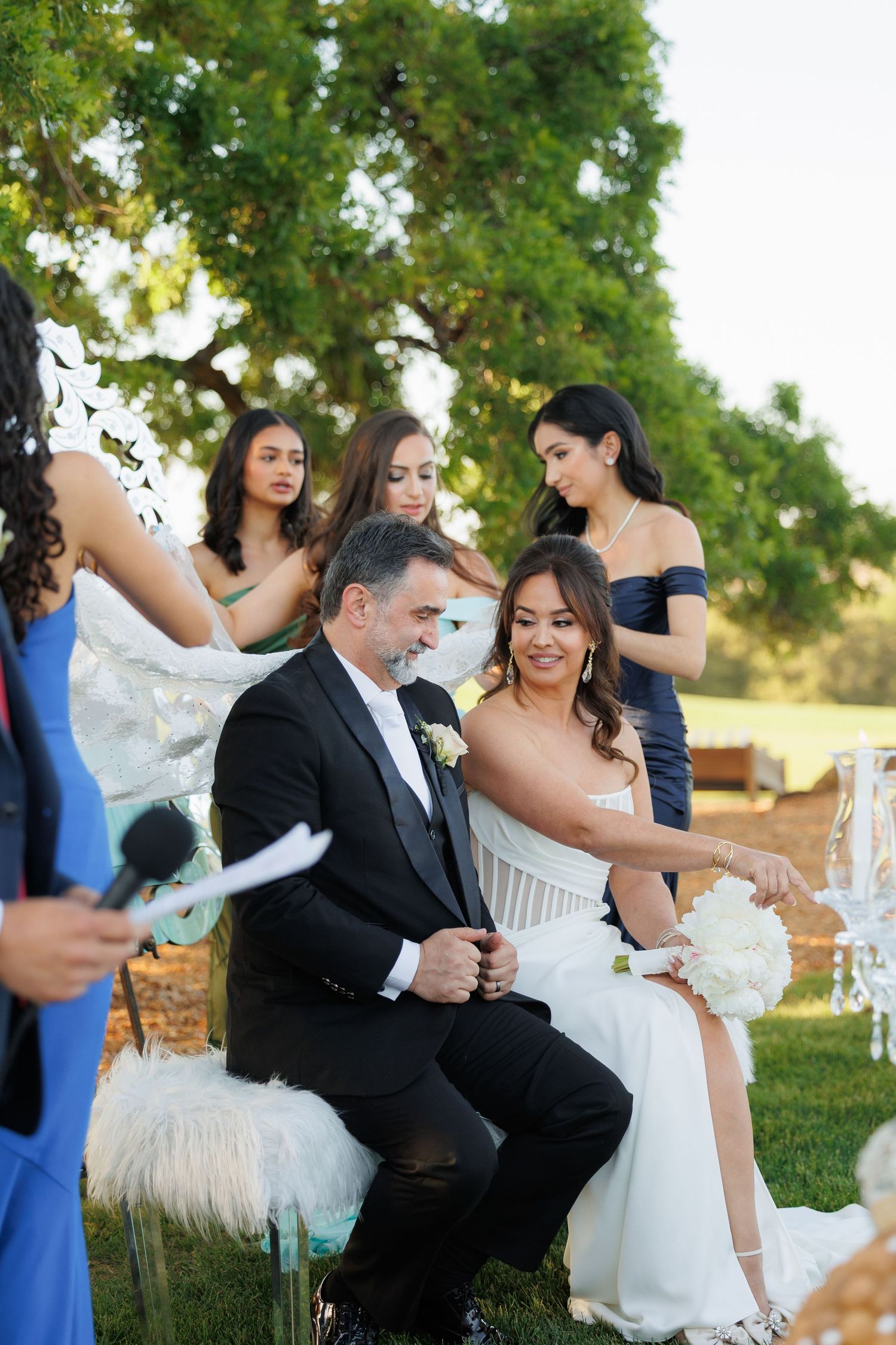 Wedding party gathered outdoors under green trees during a sunny afternoon celebration.
