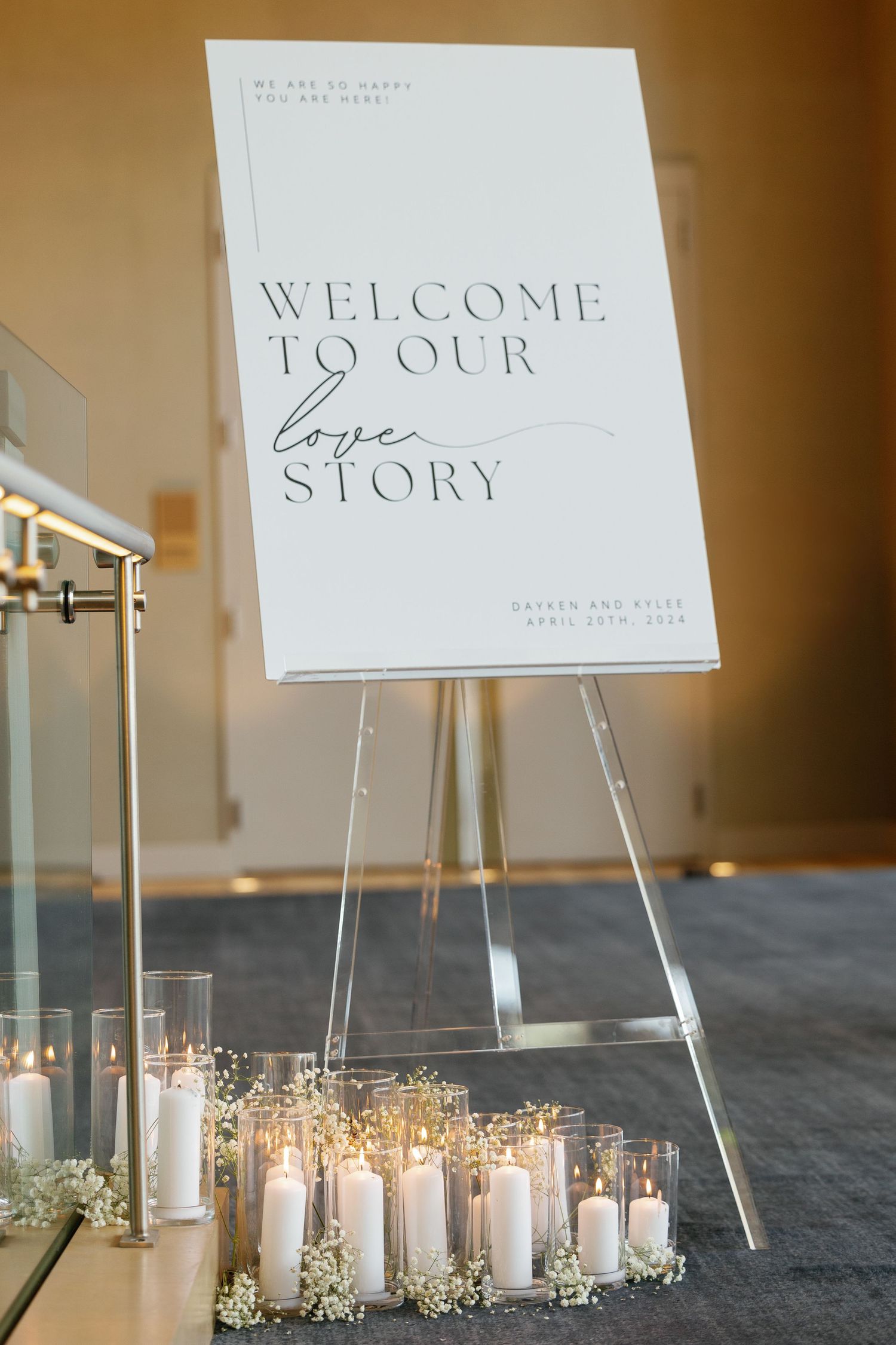 Elegant wedding welcome sign displayed on easel with glowing candles and baby's breath flowers arranged at the base.