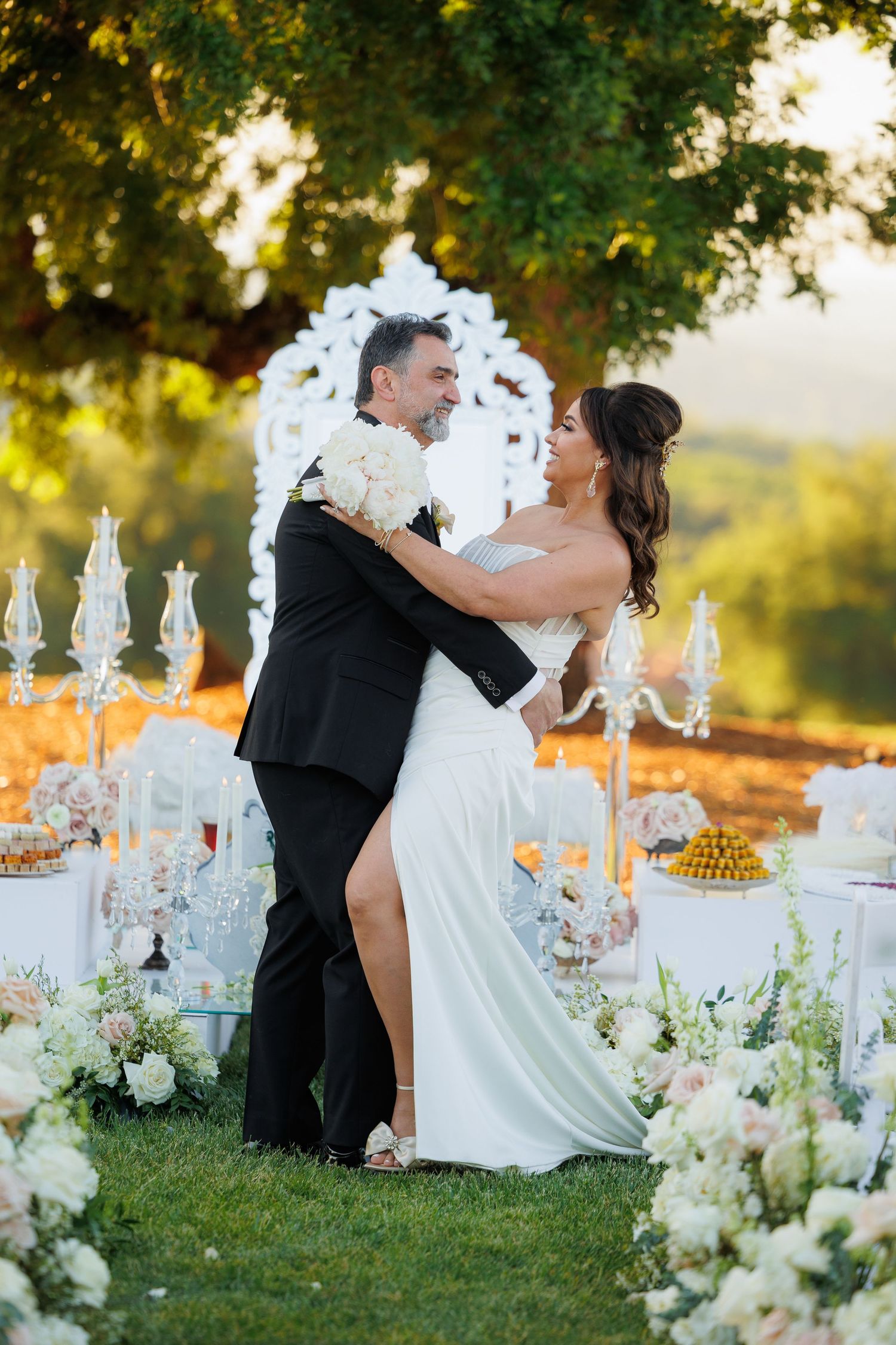 Elegant outdoor wedding reception setup with white floral arrangements and crystal candelabras at sunset.