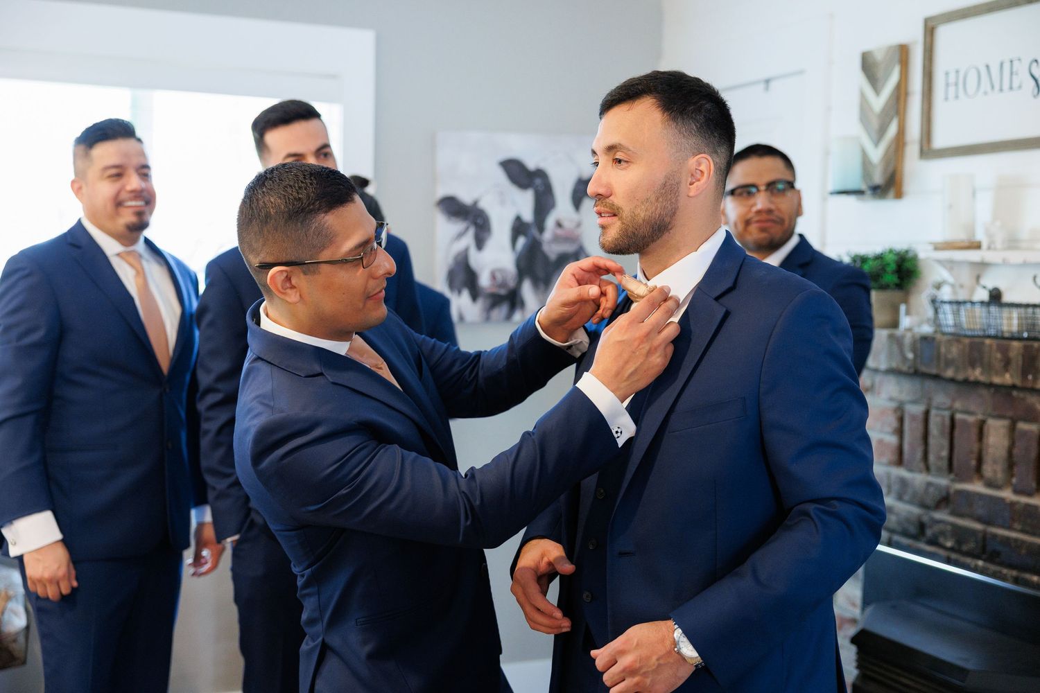 A group of groomsmen in navy blue suits laugh and socialize at a wedding celebration.