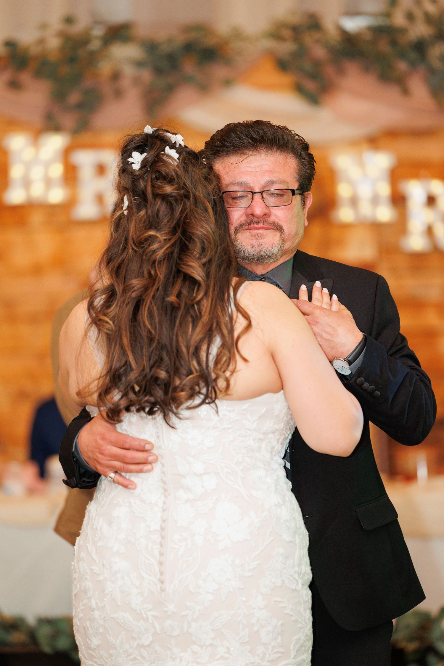 Emotional father-daughter dance moment captured during wedding reception in warm-lit venue.