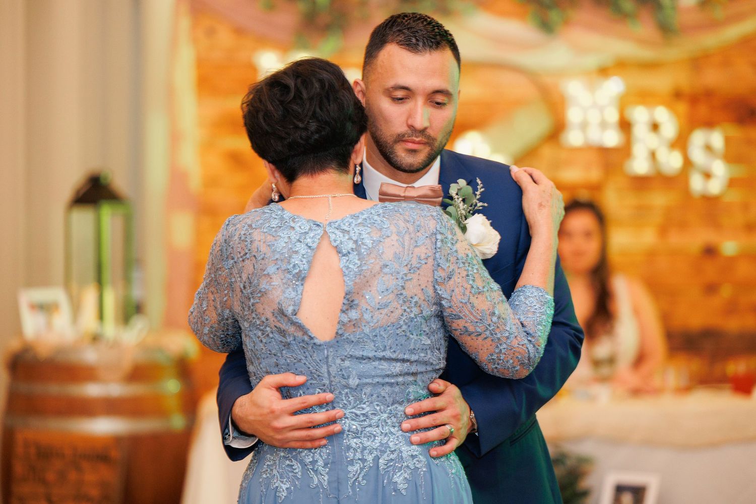 A tender moment during a wedding dance as two people embrace in formal attire, with blue lace dress and navy suit.