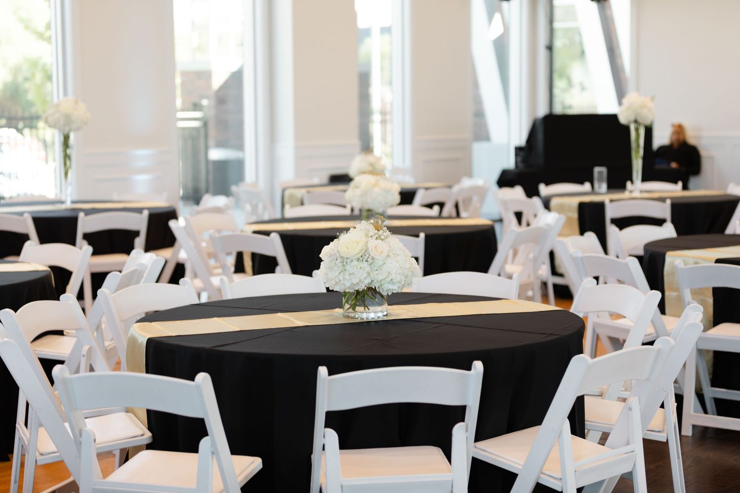 An elegant banquet hall setup with black tablecloths and white chair covers arranged in neat rows for a formal event.