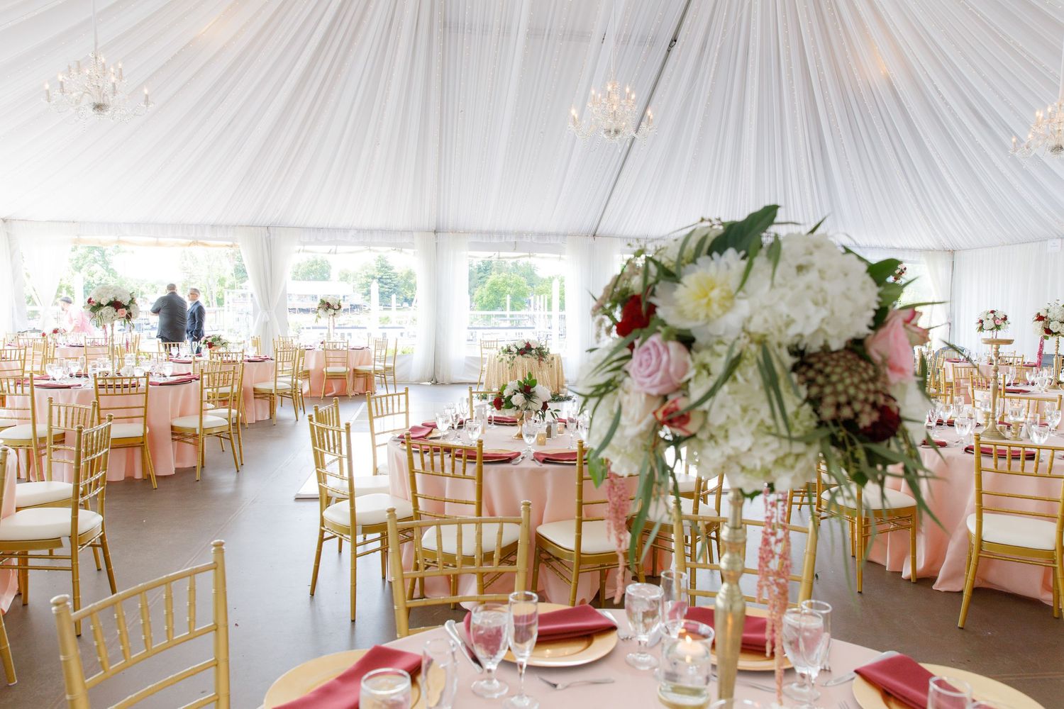 Elegant white wedding reception tent with draped fabric ceiling and golden chiavari chairs arranged around tables.