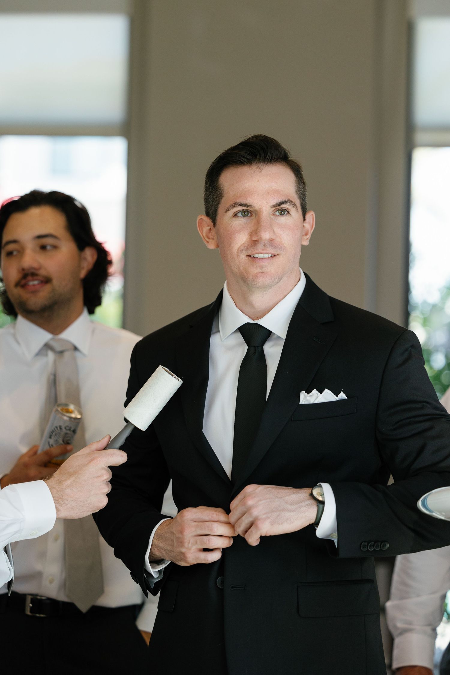 A groomsman in a black suit and tie getting ready before a wedding ceremony while being interviewed.