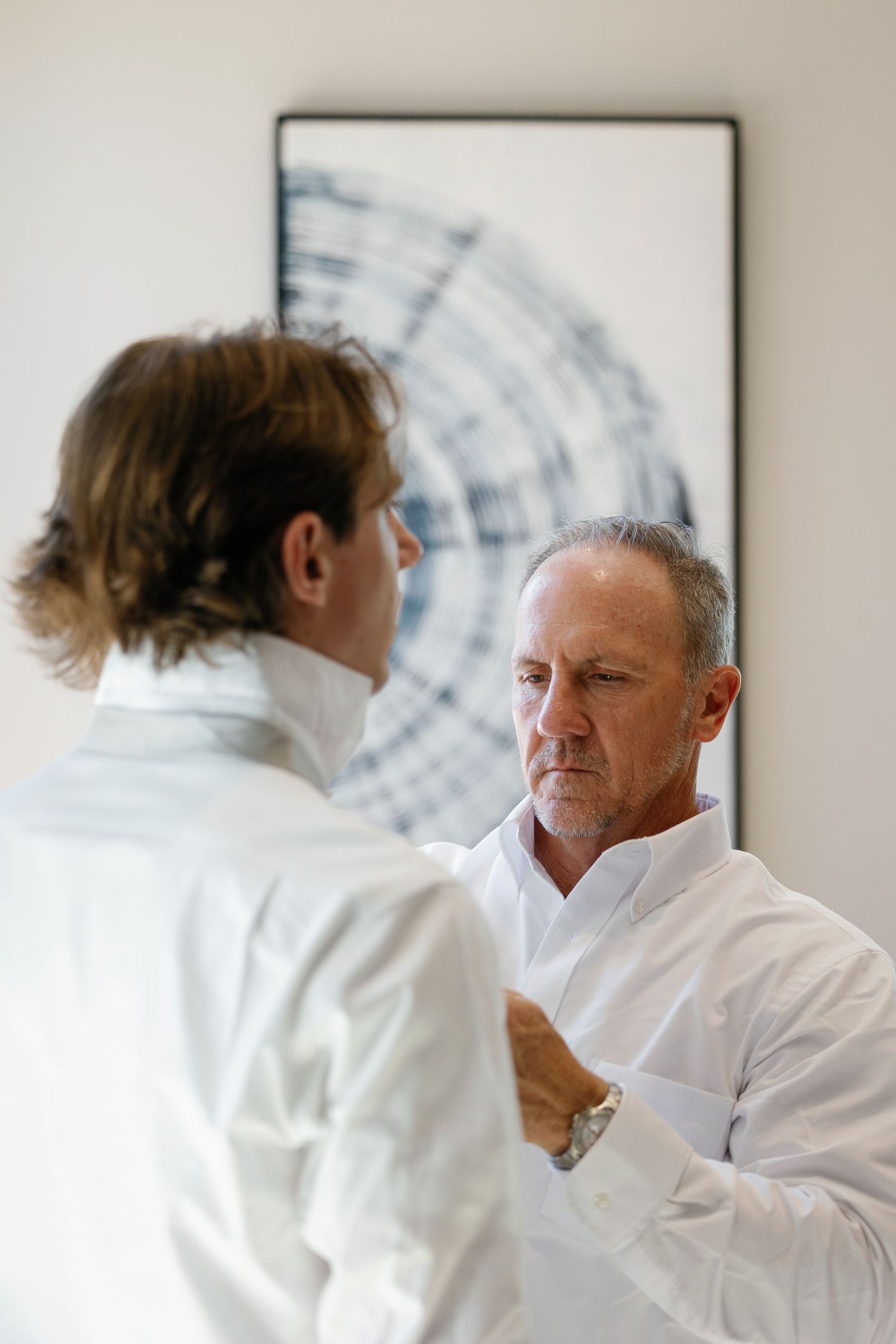 Two people in white dress shirts having a serious conversation in front of abstract wall art.