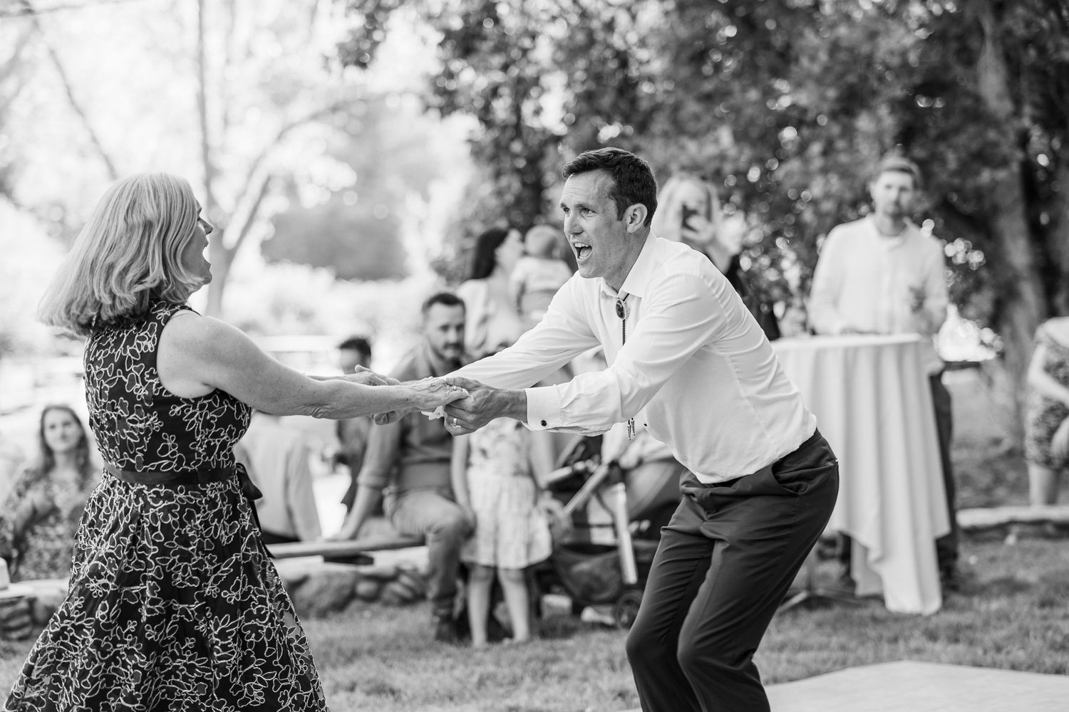Wedding guests dance and celebrate together during an outdoor reception under trees at dusk.