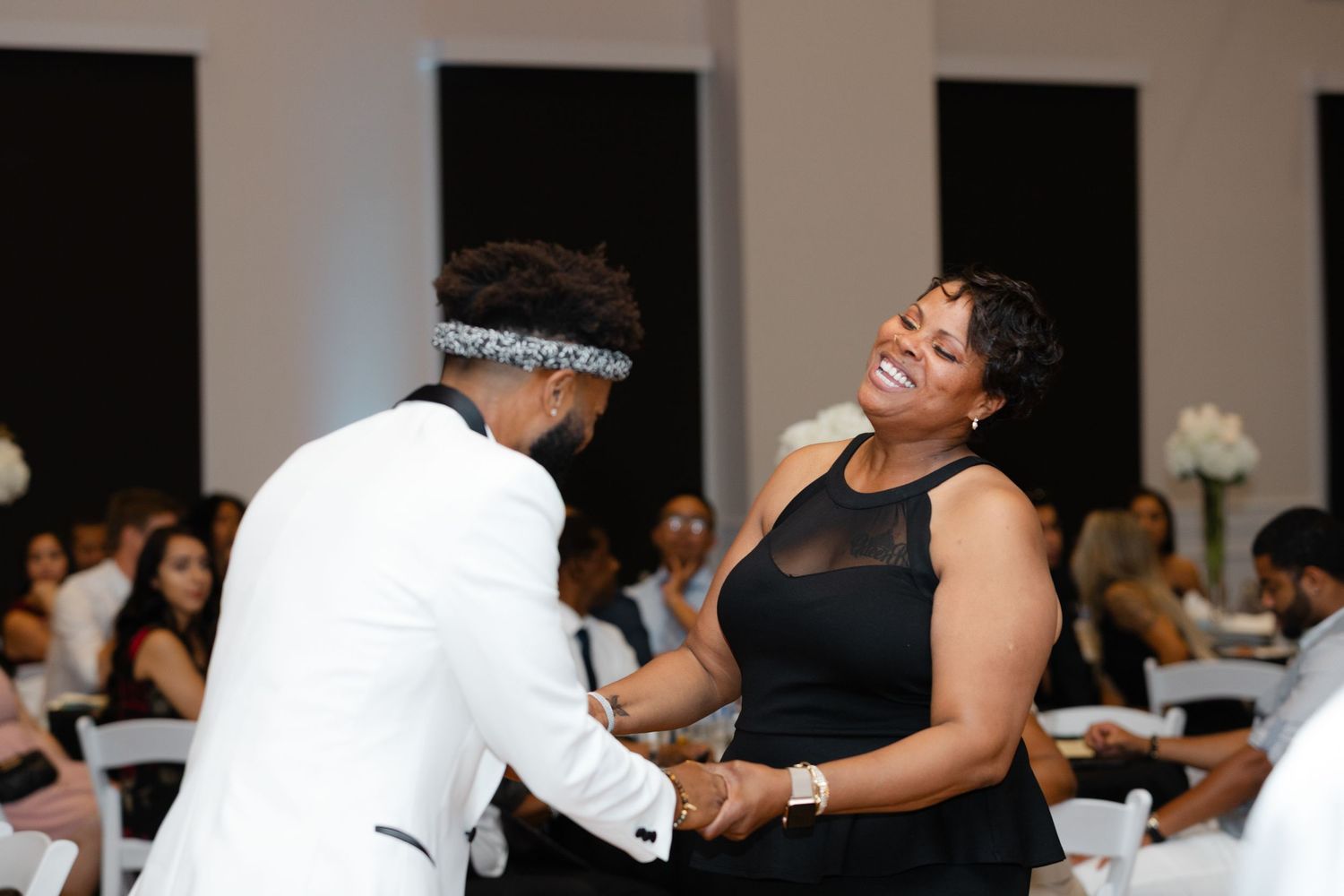 People dancing and celebrating at a wedding reception in a bright indoor venue with white decor.