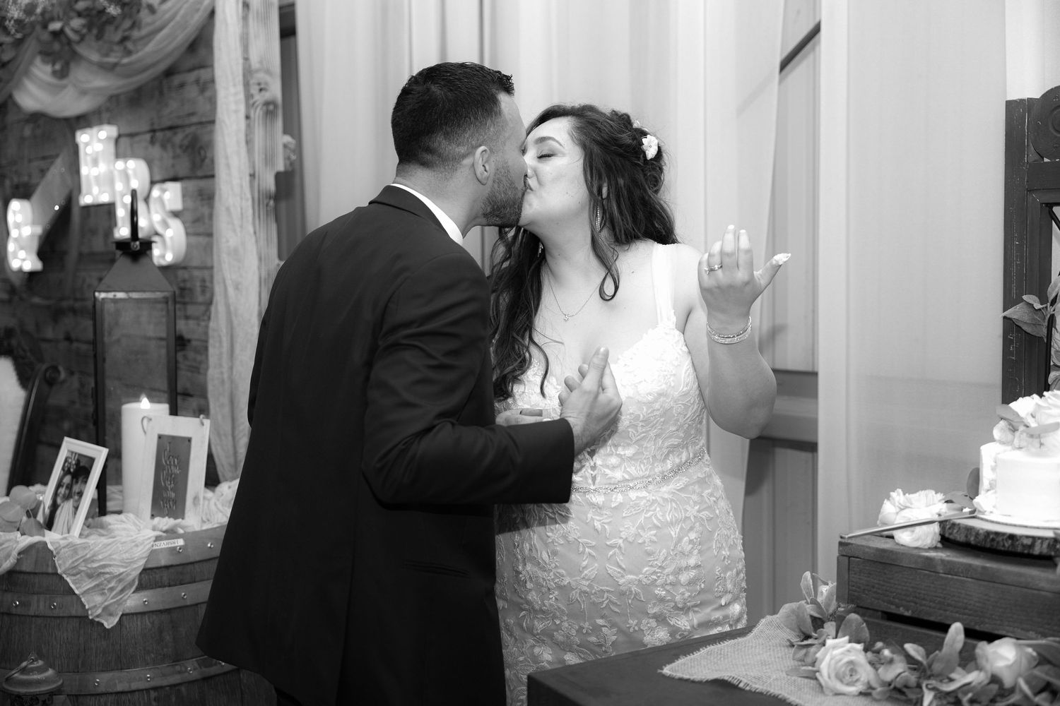 A couple shares an intimate moment at their wedding reception next to a display table in black and white photography.