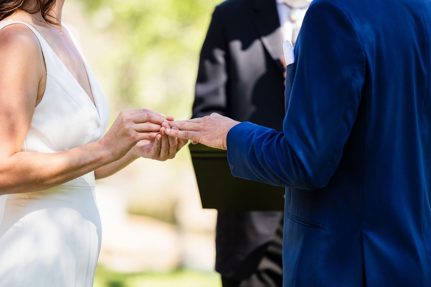 Close-up shot of exchanging wedding rings during an outdoor ceremony with white dress and navy suit details.