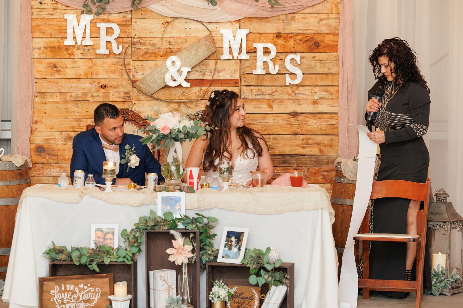 Rustic wooden wedding reception venue with white tablecloths and greenery garland decorations along tables.