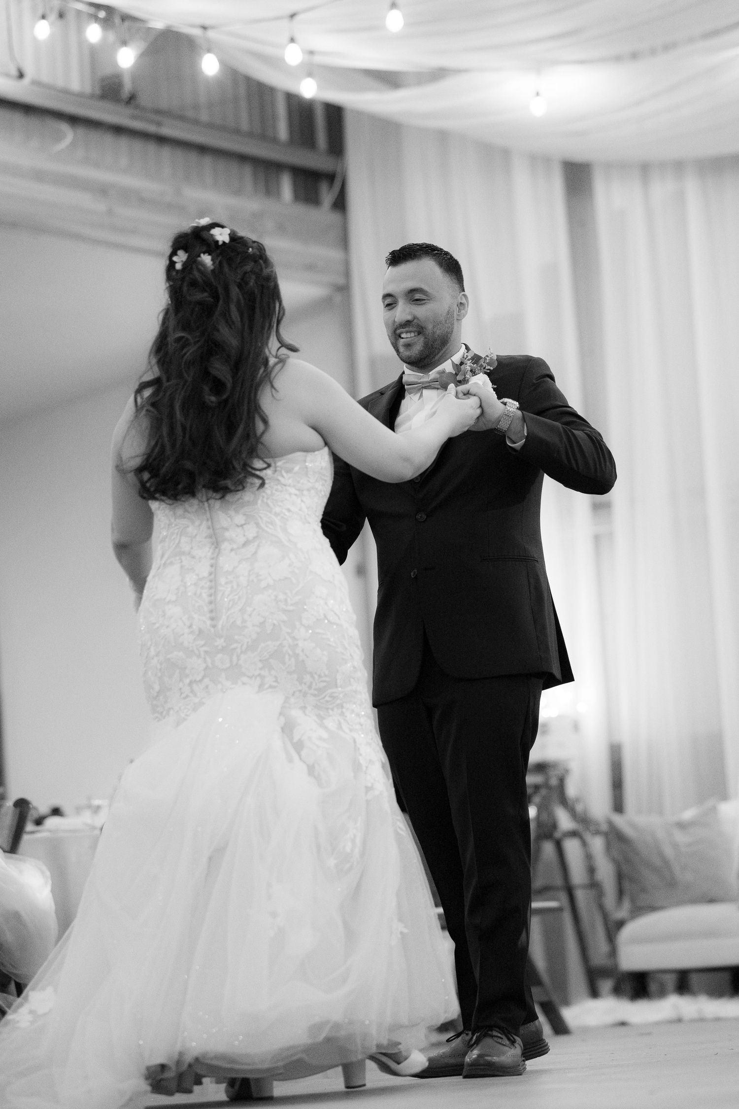 A bride and groom share their first dance together at a wedding reception in an elegant white-draped ballroom.