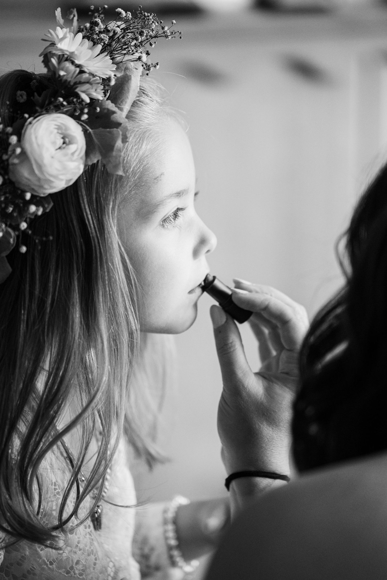Black and white photo series showing makeup application with flowers in hair during a bridal preparation session.