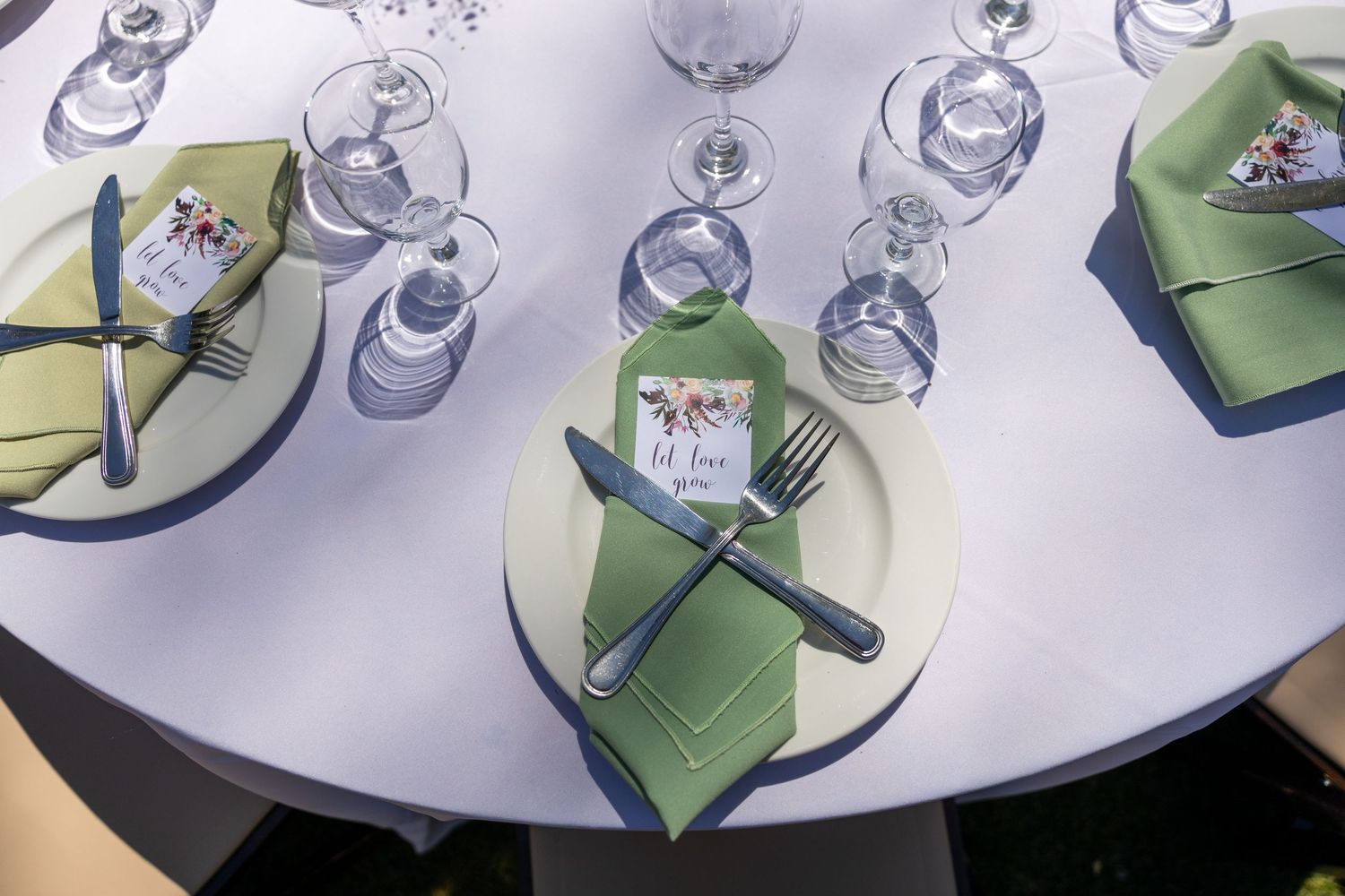 Overhead view of multiple wine glasses arranged in a circular pattern on a white surface with green napkins.