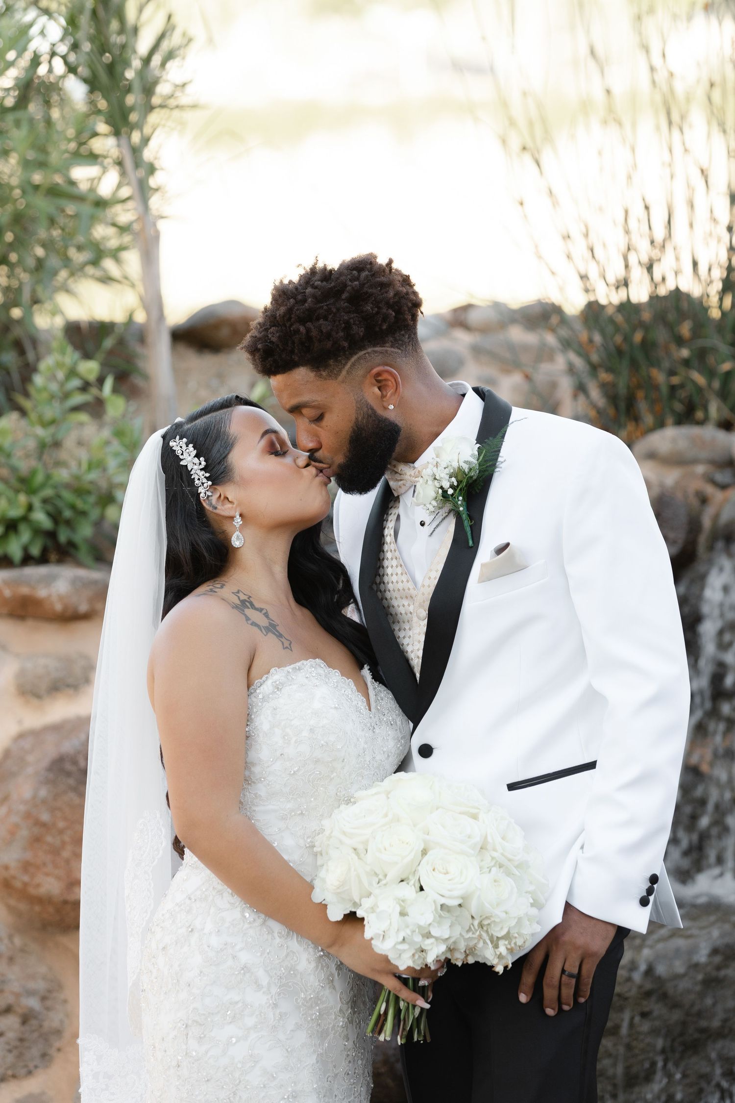 A romantic wedding portrait of a couple sharing an intimate moment with a white bouquet against a natural outdoor backdrop.