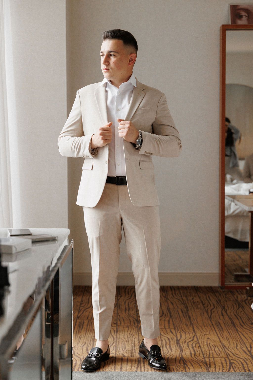 Multiple views of someone posing in a cream-colored suit against a minimalist interior setting.