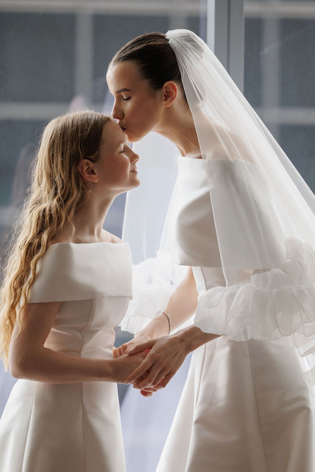 A romantic wedding sequence showing a couple in white embracing near a window with flowing veil and soft lighting.