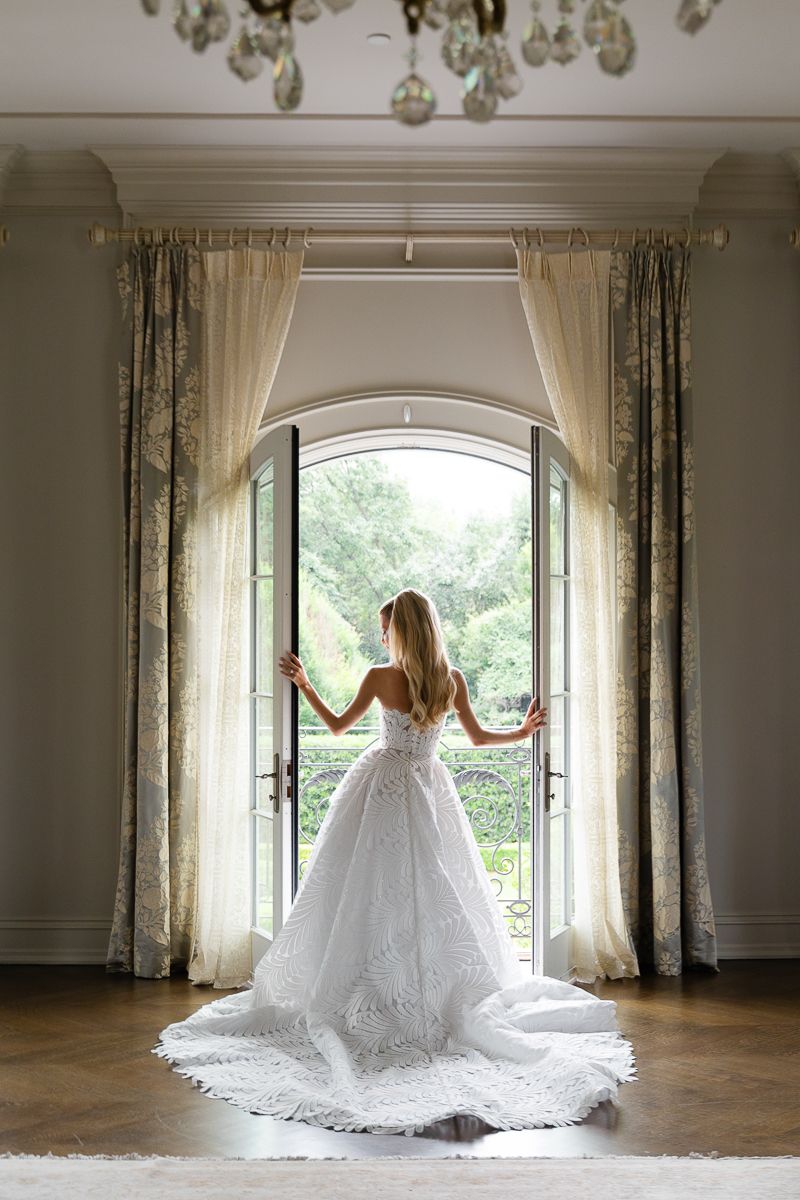 A wedding dress silhouette twirls gracefully in an elegant room with arched windows and flowing curtains.