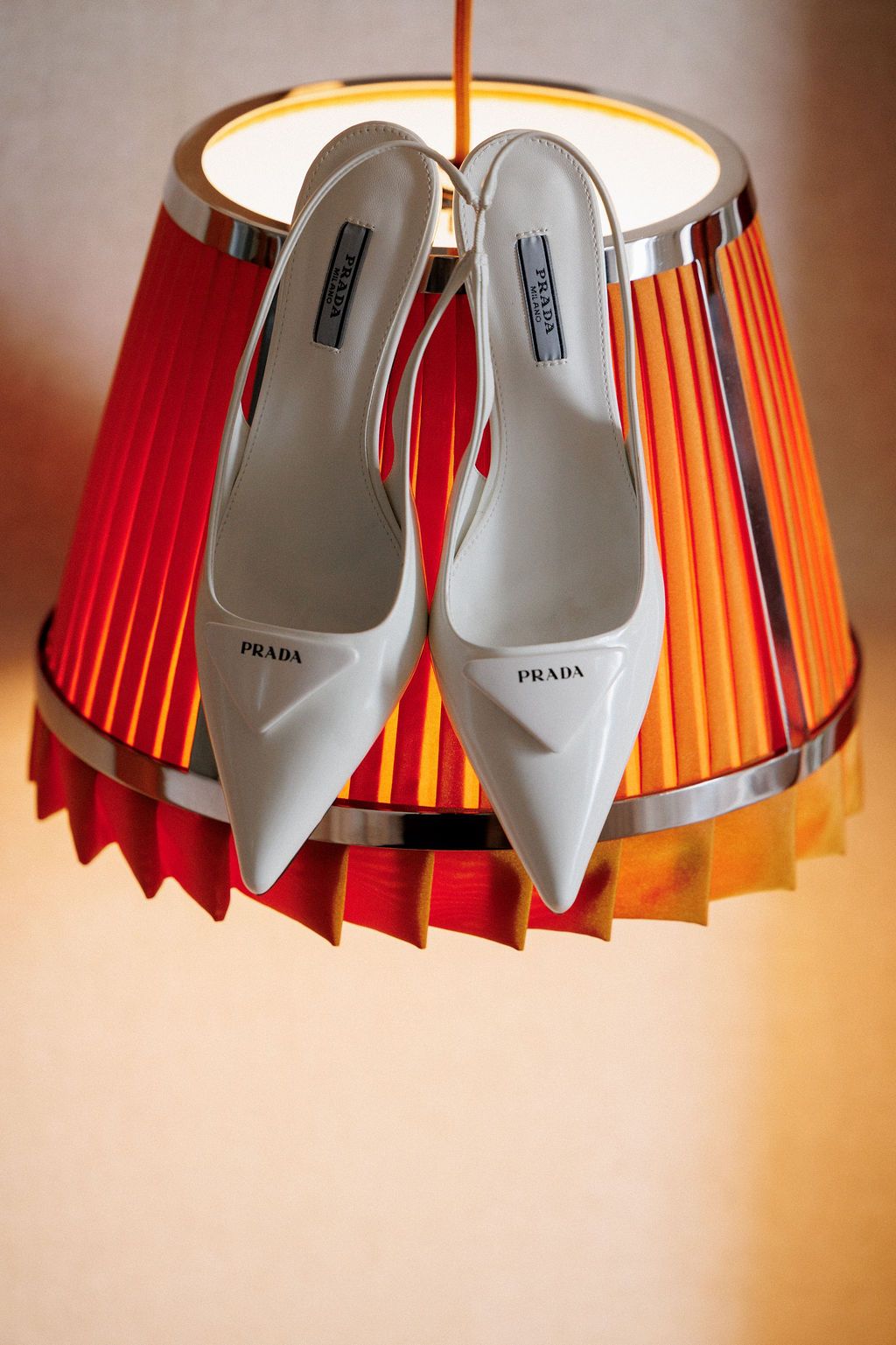 A sequence of Prada white high heel shoes displayed under an orange pleated lampshade.