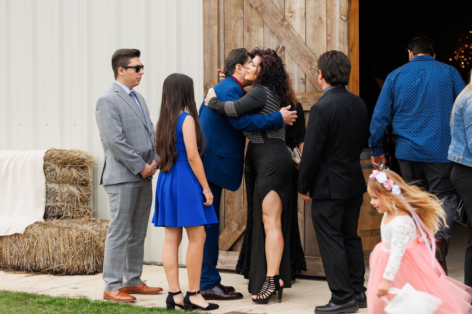 A group of wedding guests gathered outside a rustic venue wearing formal attire in blue and dark colors.