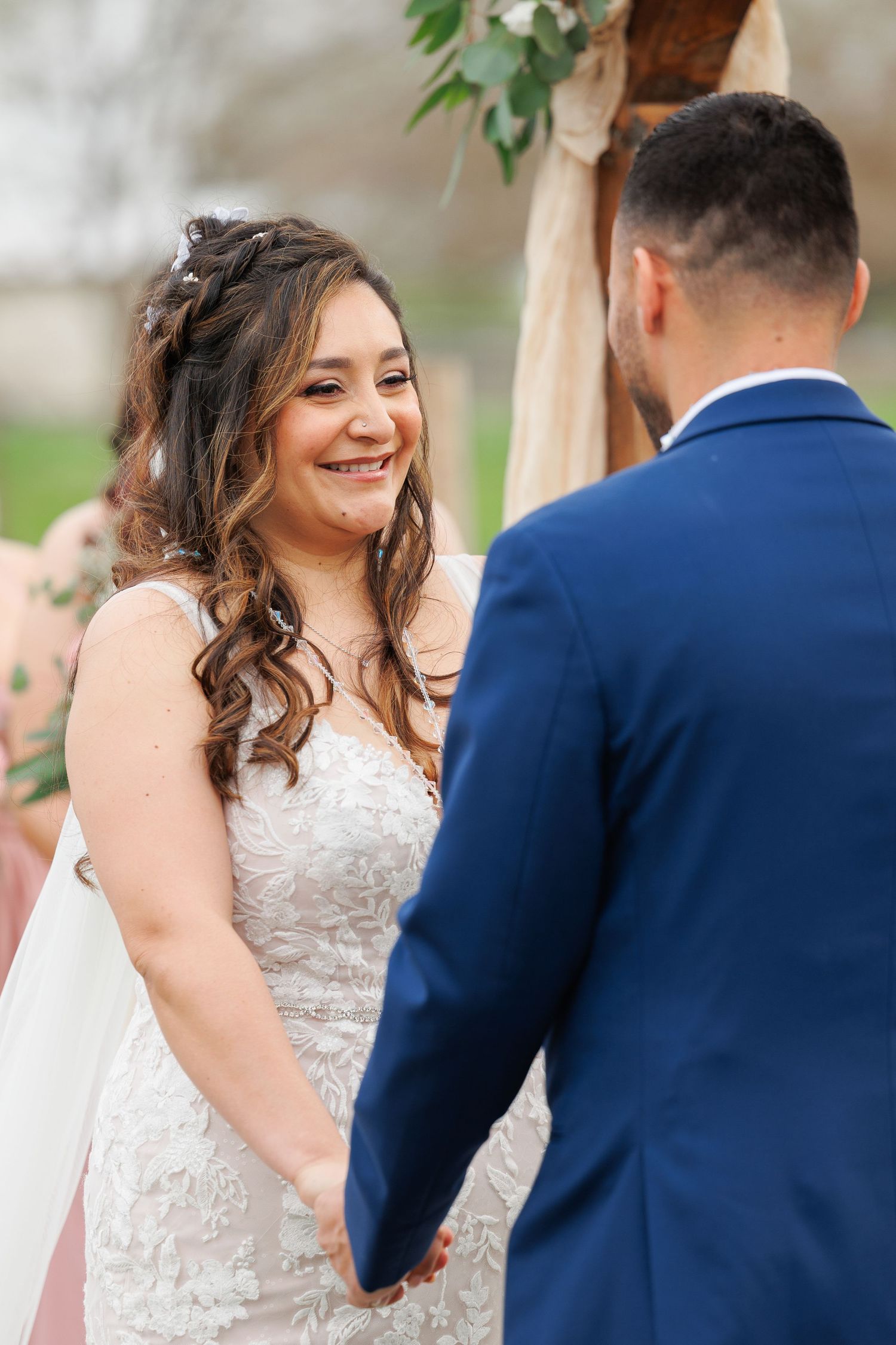 A bride in a white lace dress shares joyful moments with her groom in a navy suit during their outdoor wedding ceremony.