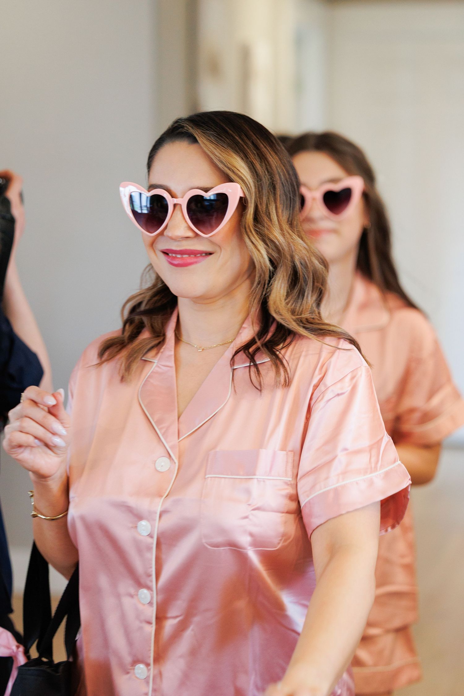A person wearing pink heart-shaped sunglasses and a satin pajama top smiles in a candid photo series.