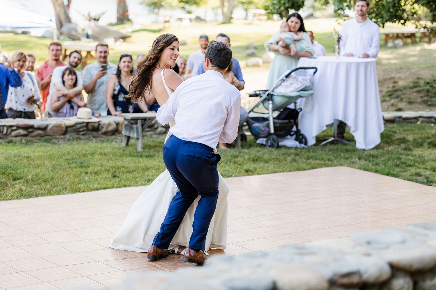 Guests gather at an outdoor wedding reception with white tablecloths and natural surroundings in a park setting.