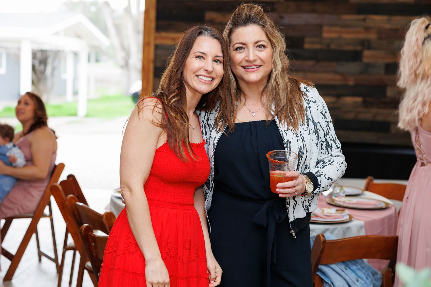 People in formal attire socialize and enjoy drinks at an indoor event with wood paneled walls.