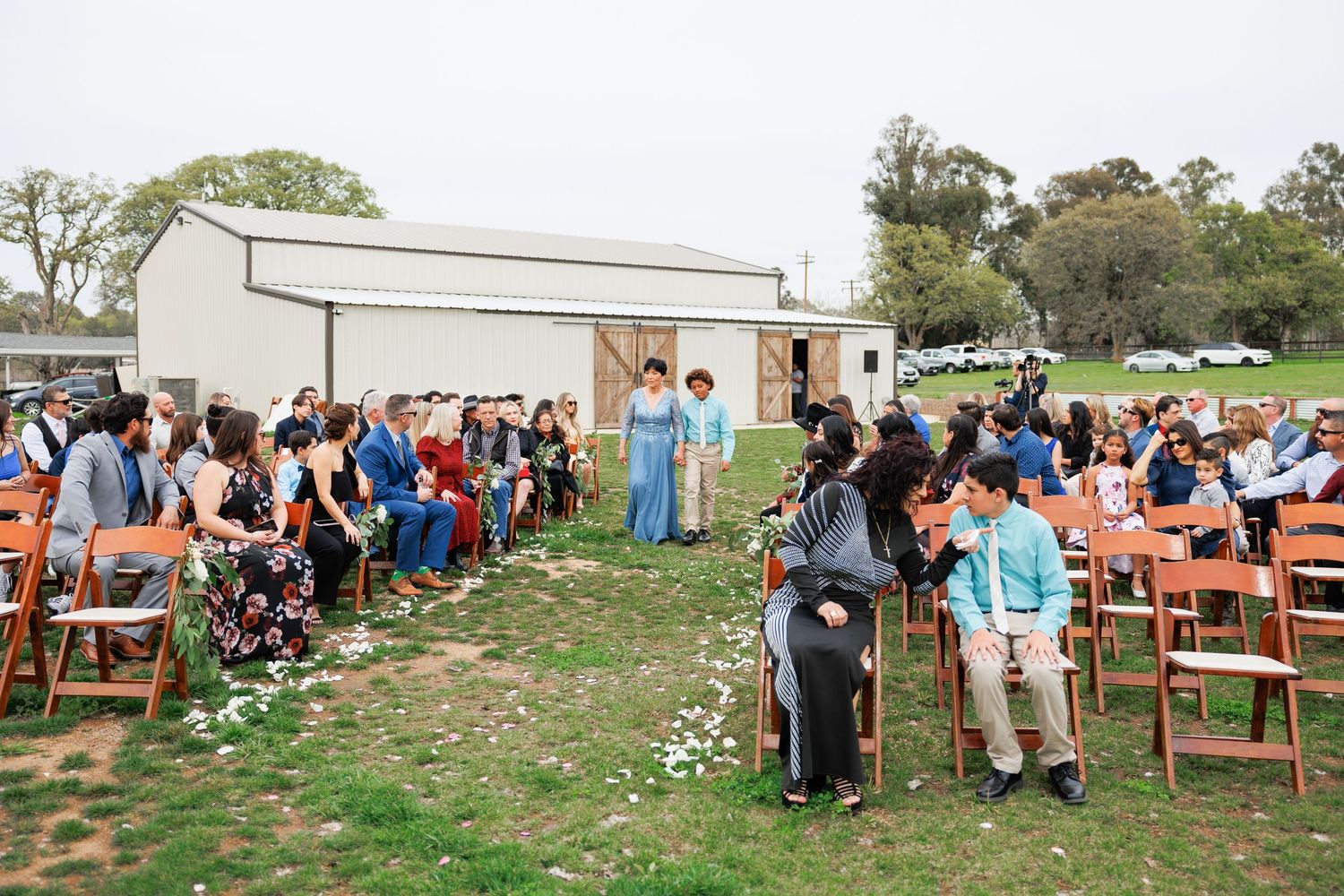 A panoramic view of outdoor wooden chairs arranged for a rustic wedding ceremony in a grassy field.