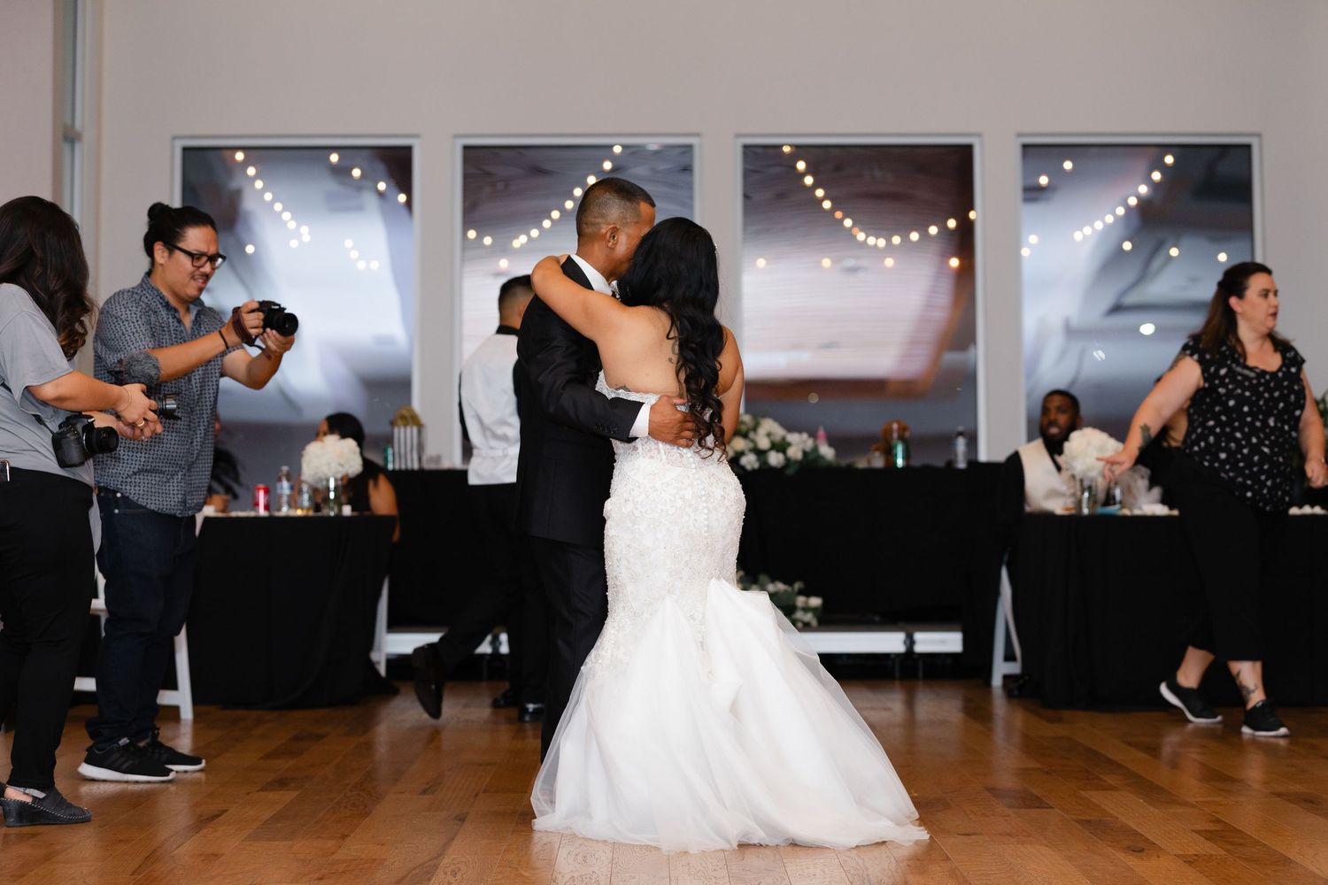 Dancers twirl across a ballroom floor during a wedding reception as string lights sparkle overhead.