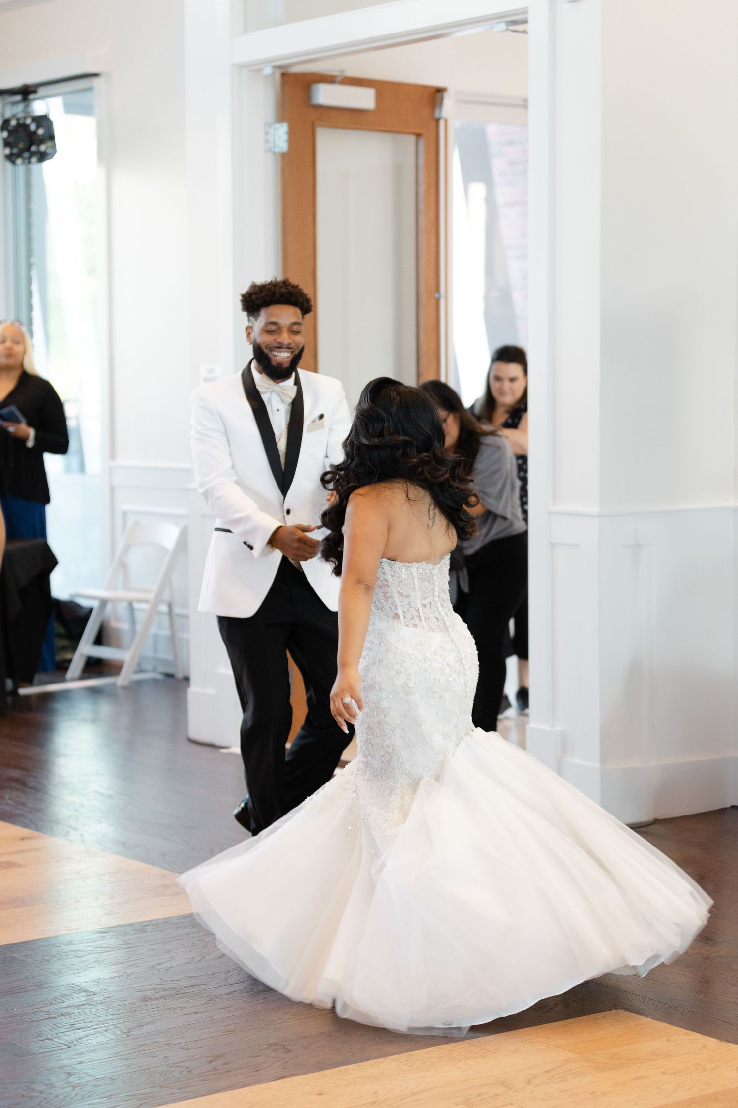 A couple performs an elegant twirling dance move in formal wedding attire on a light hardwood floor.