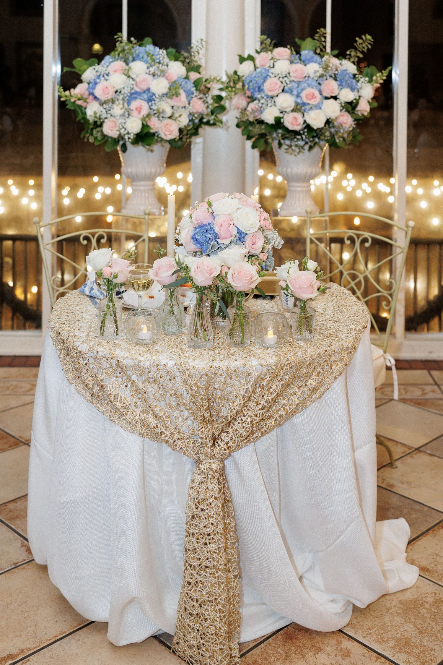 Elegant wedding table with blue and pink floral arrangements on a sequined gold tablecloth.