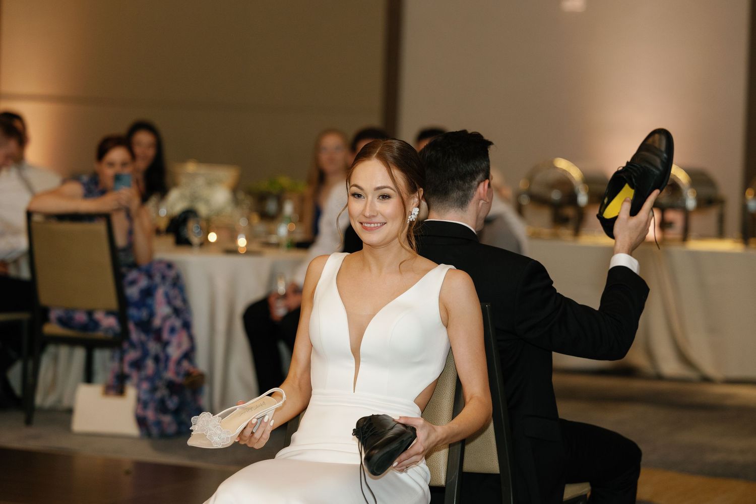 A couple shares a romantic dance at their wedding reception, surrounded by guests in an elegant indoor venue.