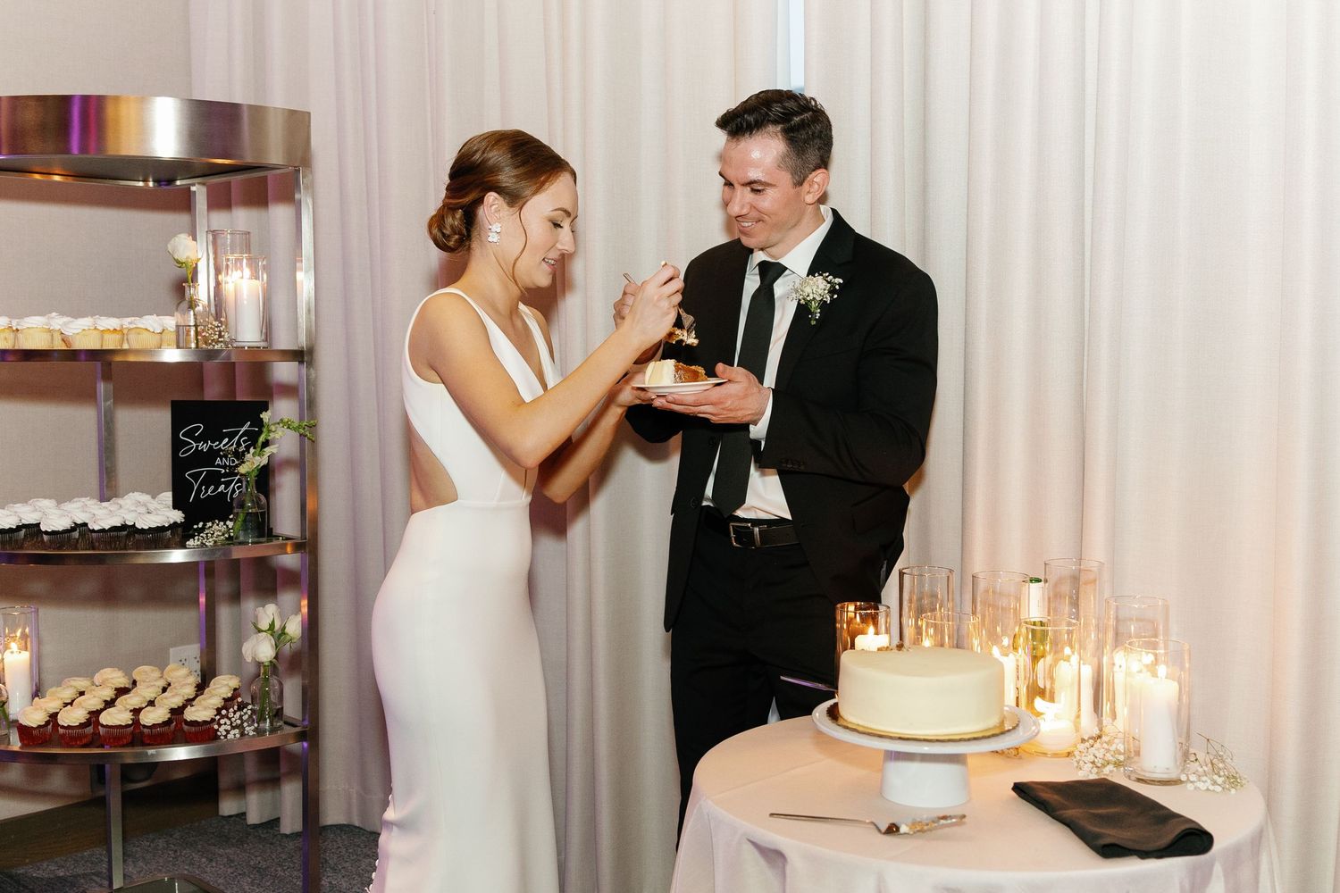 A bride and groom share an intimate moment while cutting their wedding cake at an elegant reception with candlelight.