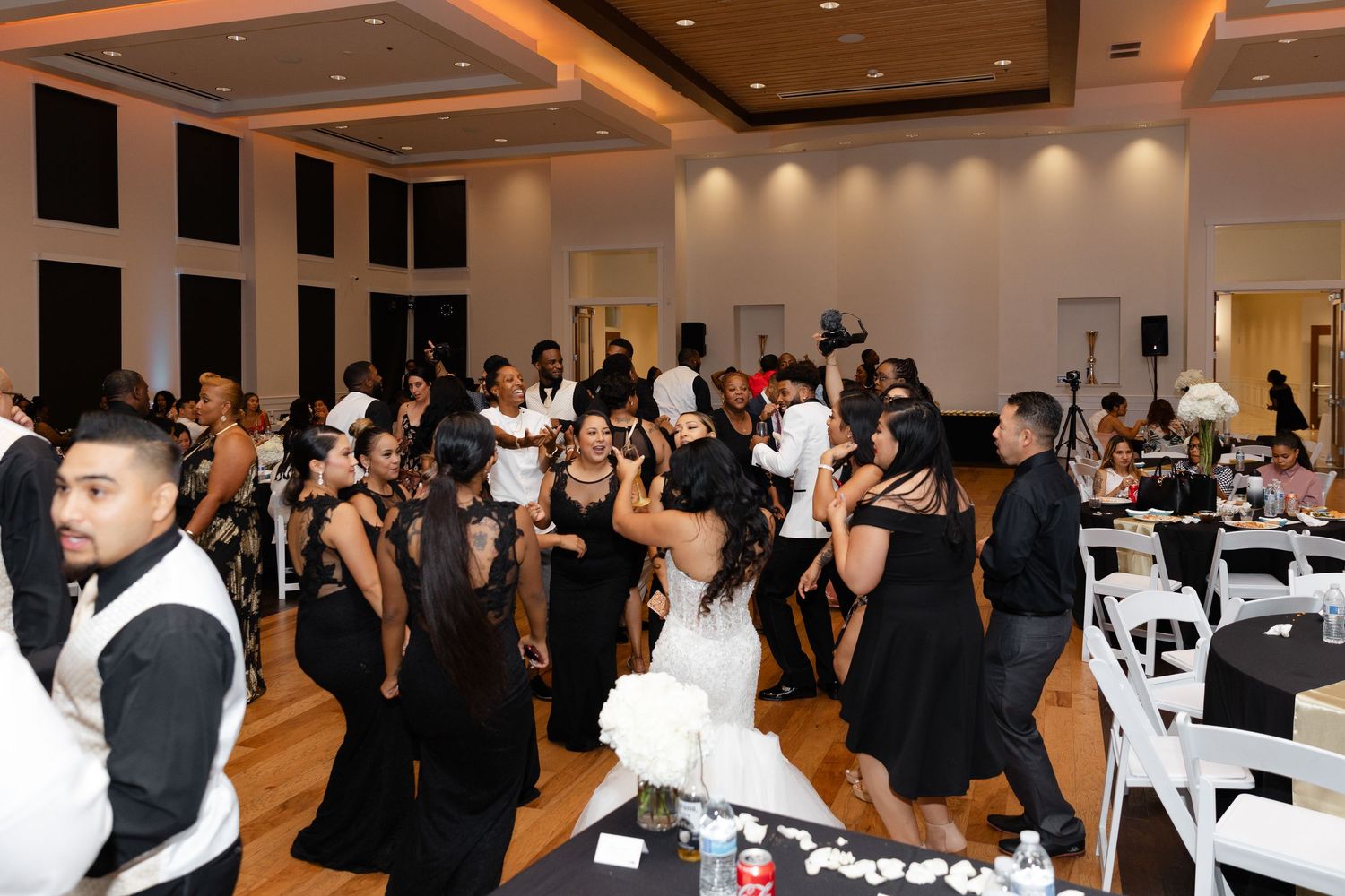 Wedding guests dance together on a wooden dance floor at an elegant reception with black and white formal attire.
