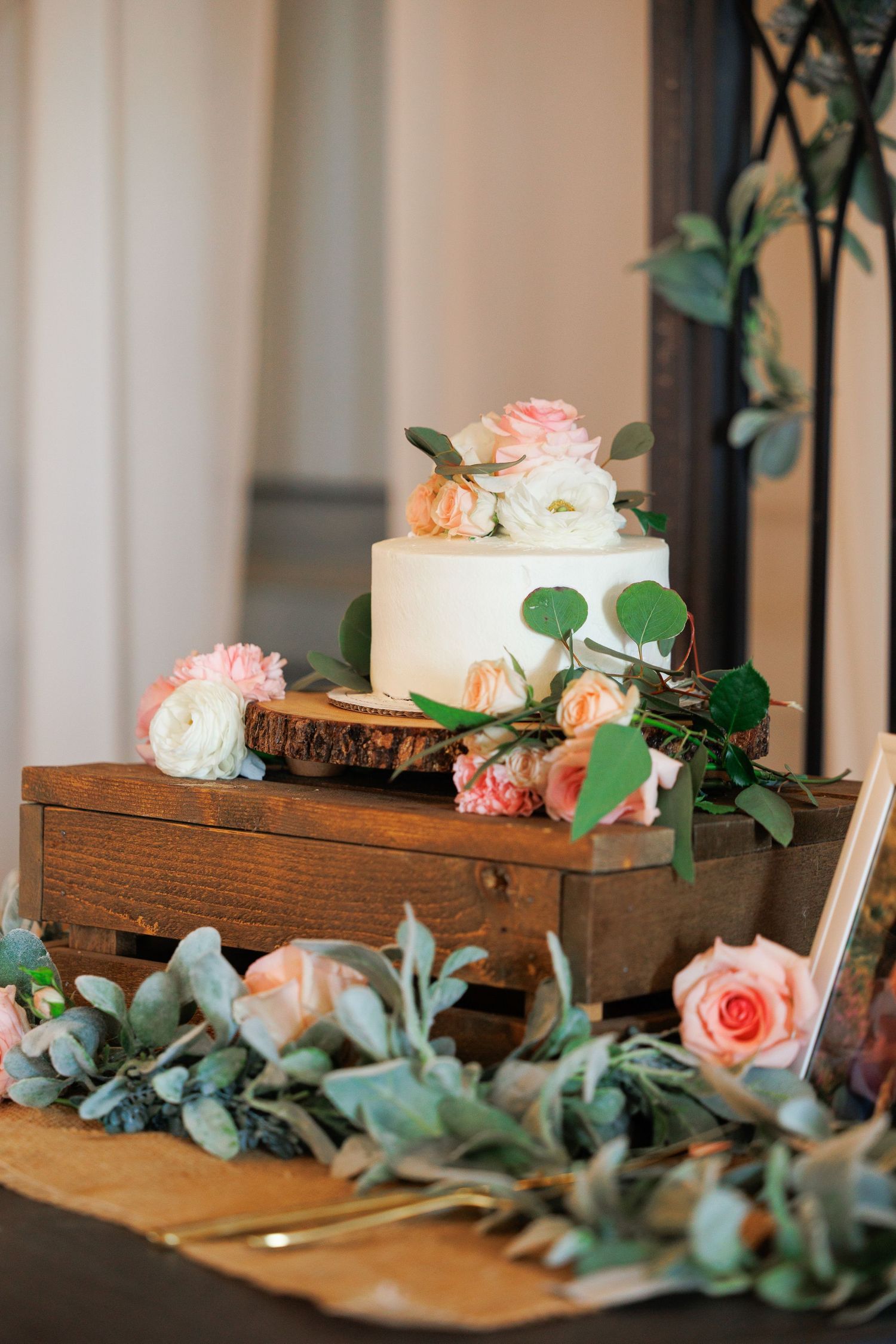 White pillar candles arranged on rustic wooden boxes with pink roses and eucalyptus greenery for wedding decor.