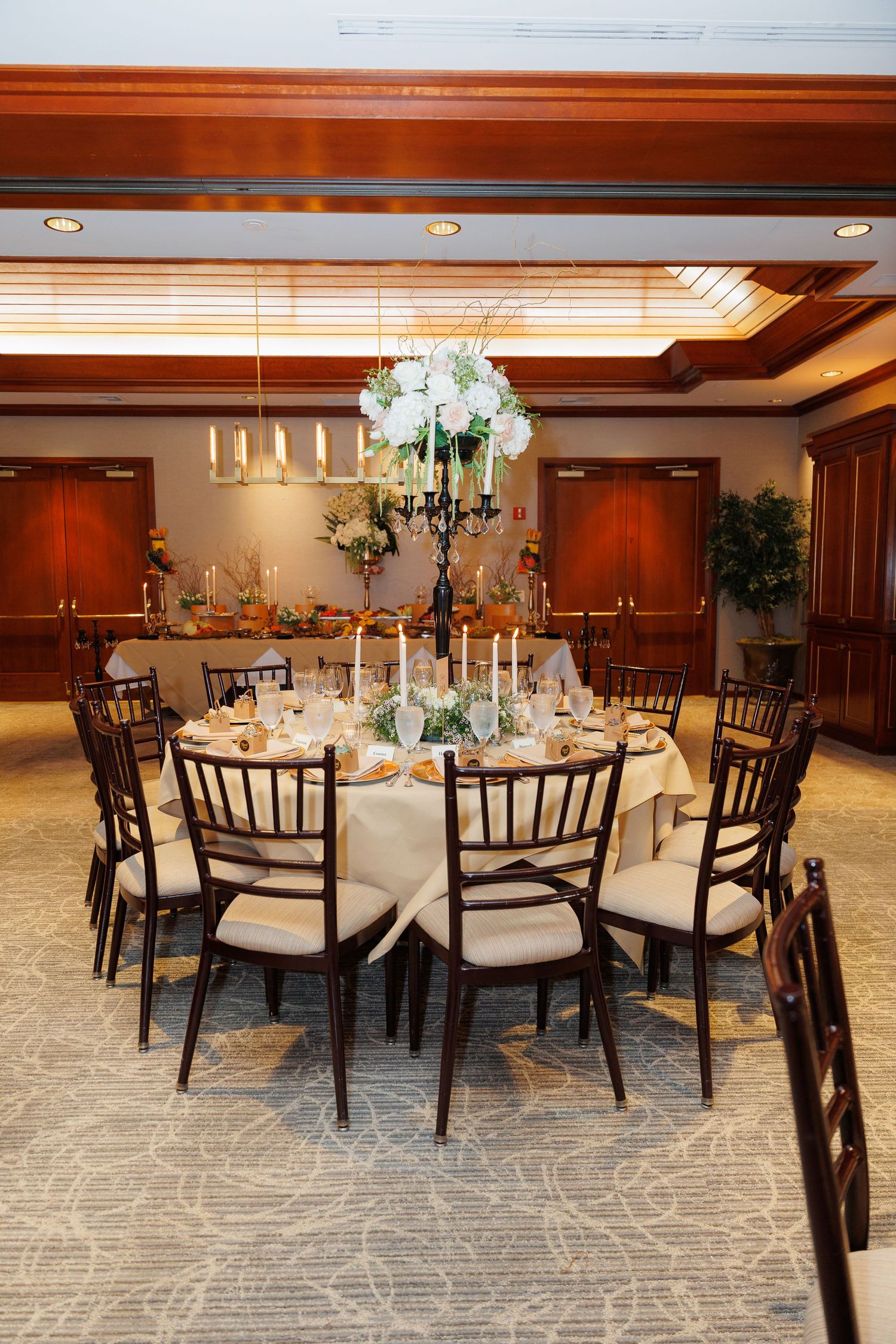 Elegant wedding reception table with white hydrangea centerpiece, candelabra, and dark chiavari chairs in a wood-paneled room.