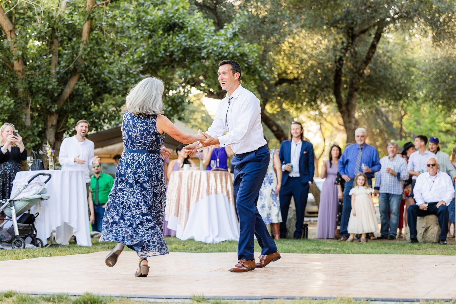 A couple dances together at an outdoor wedding reception while guests watch from the background.