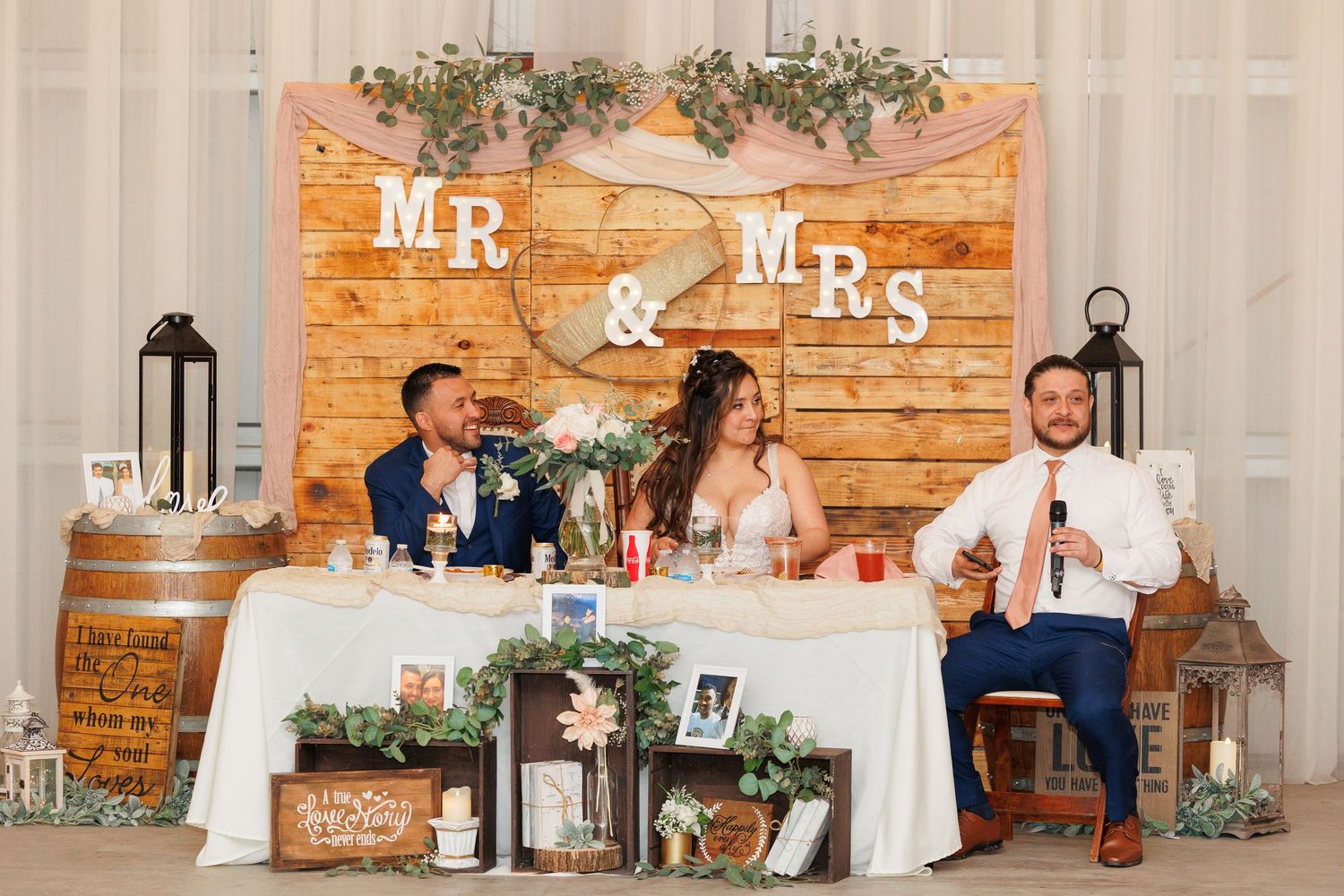 A rustic wedding reception venue with exposed brick walls, white drapes, and decorative Mr & Mrs signage.