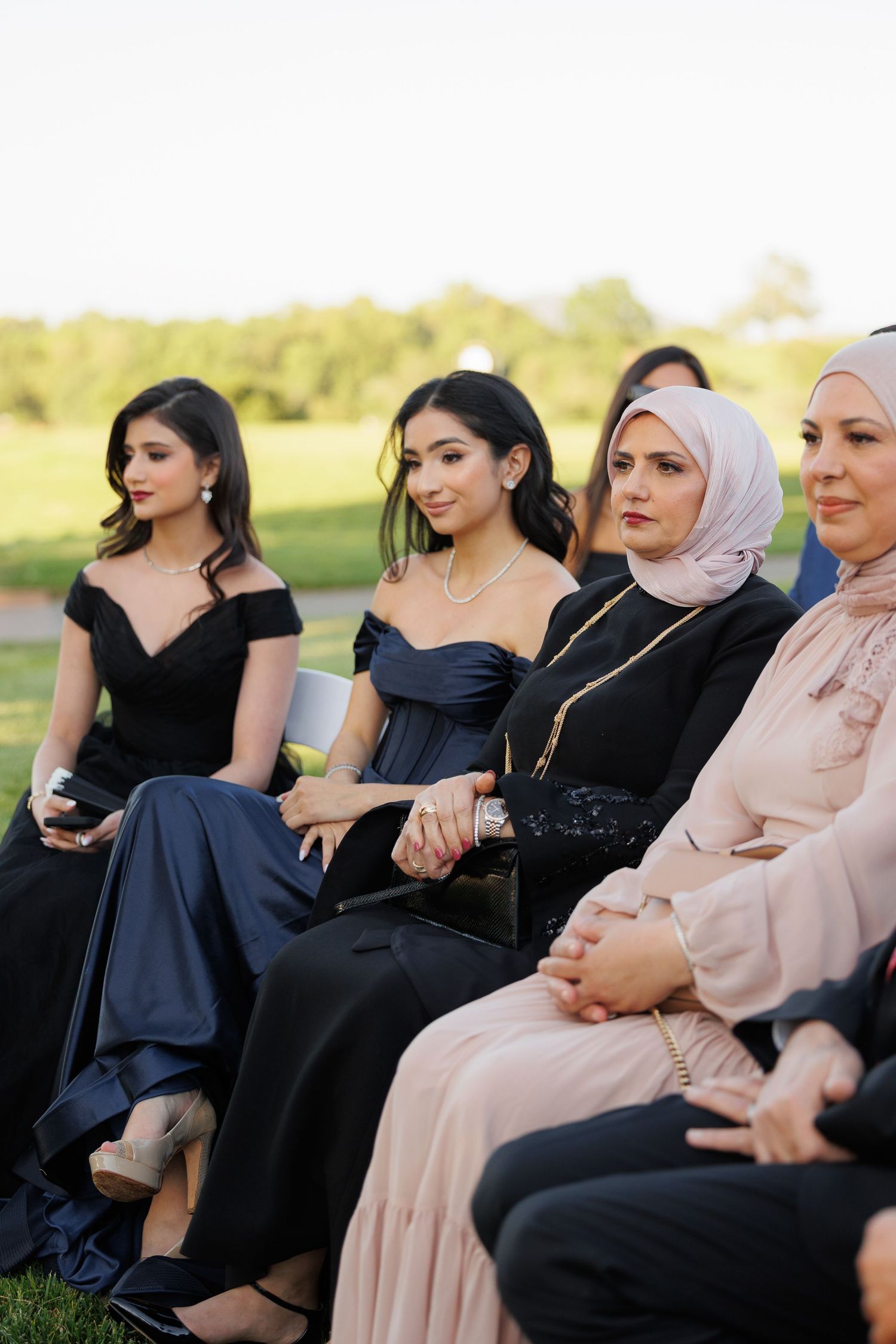 A group of women in formal black and beige attire sit together outdoors during a special event.
