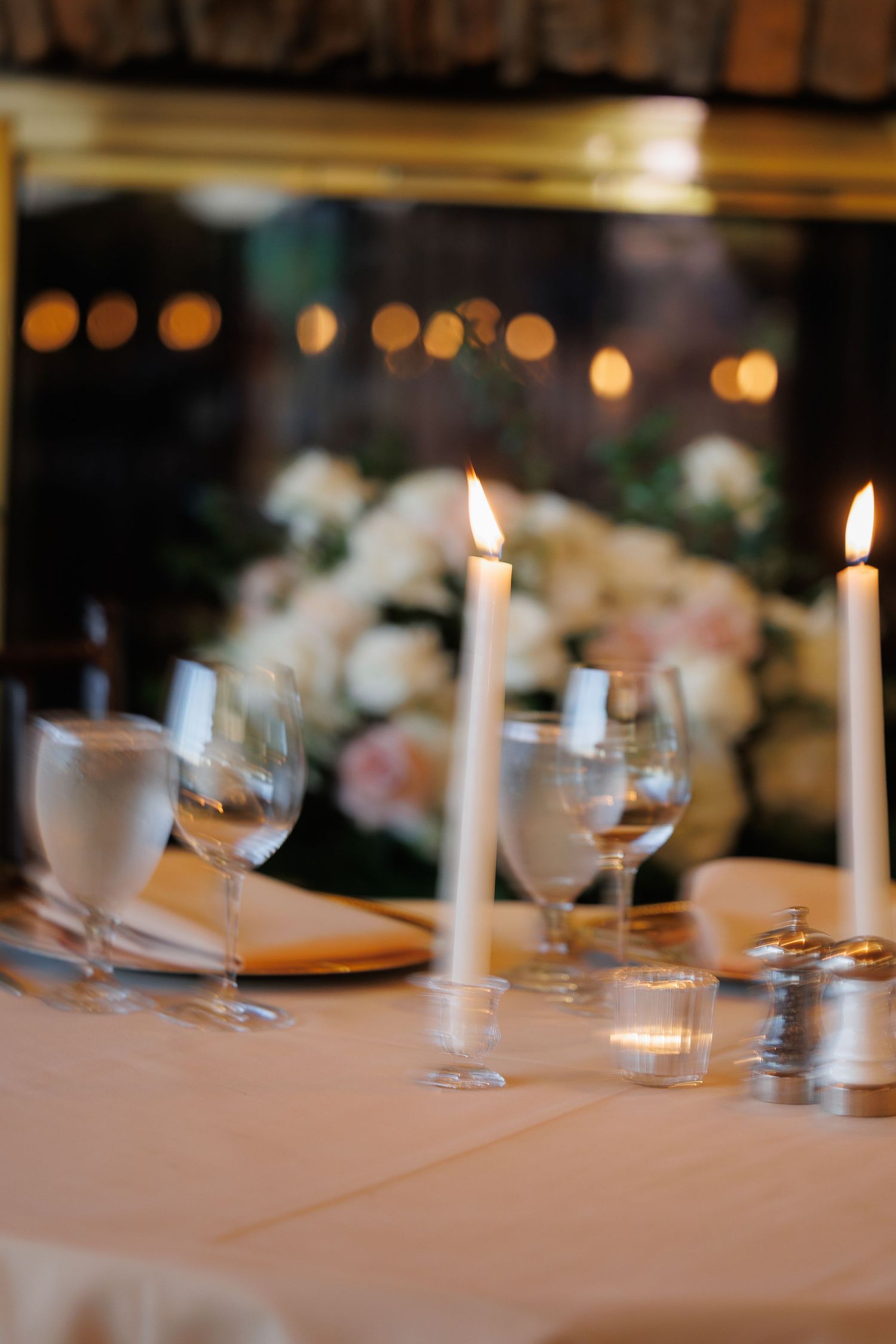 Elegant dining table setting with white linens, glowing candles, and wine glasses creating a romantic atmosphere.