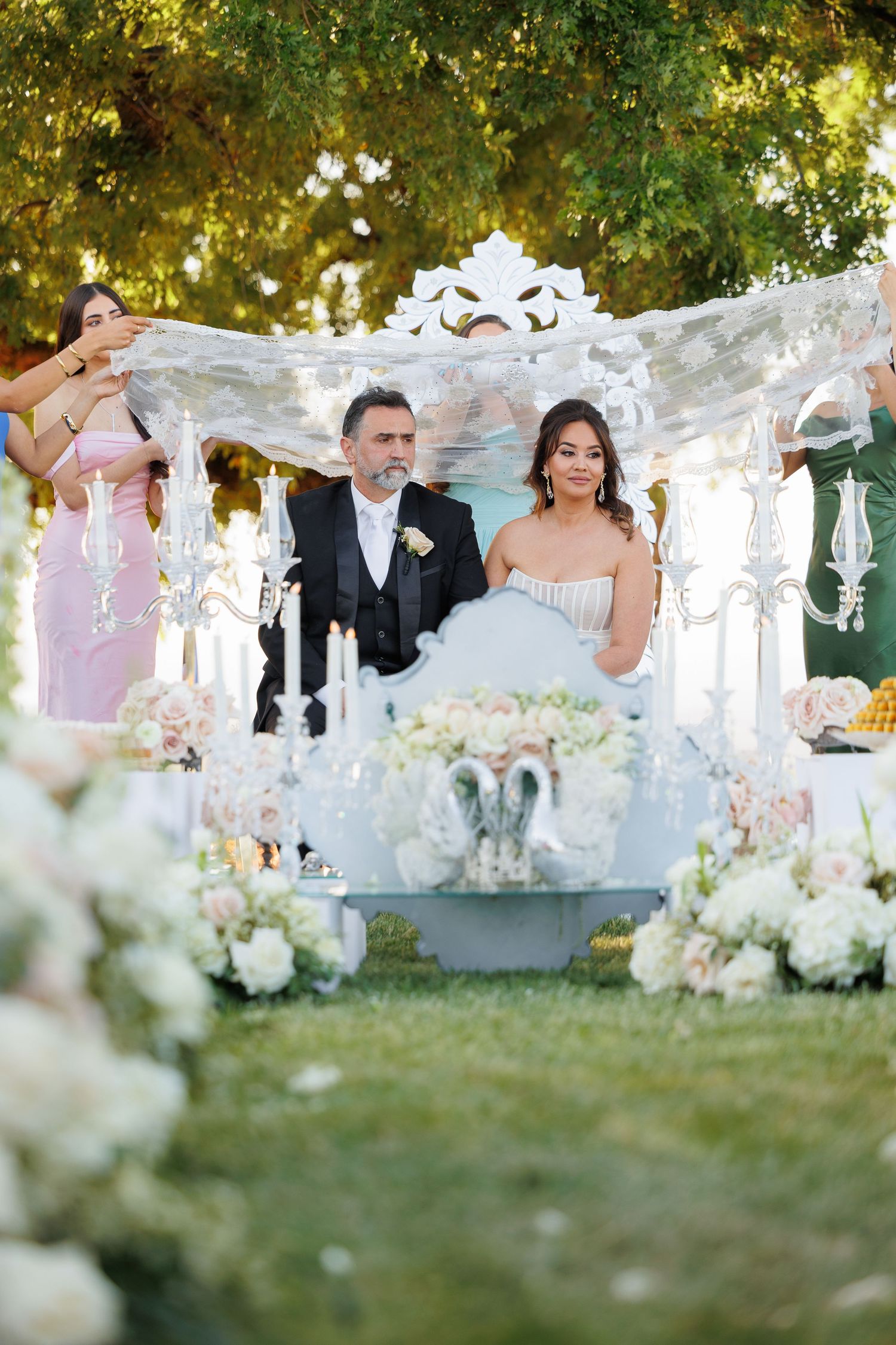 A romantic outdoor wedding ceremony setup with white draping, floral arrangements and chairs on a sunny day.