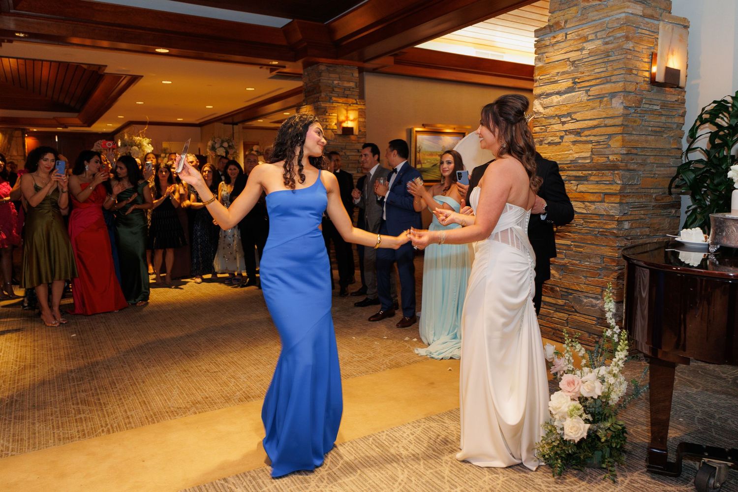Wedding guests dancing and celebrating together in an elegant stone-walled venue with warm lighting.
