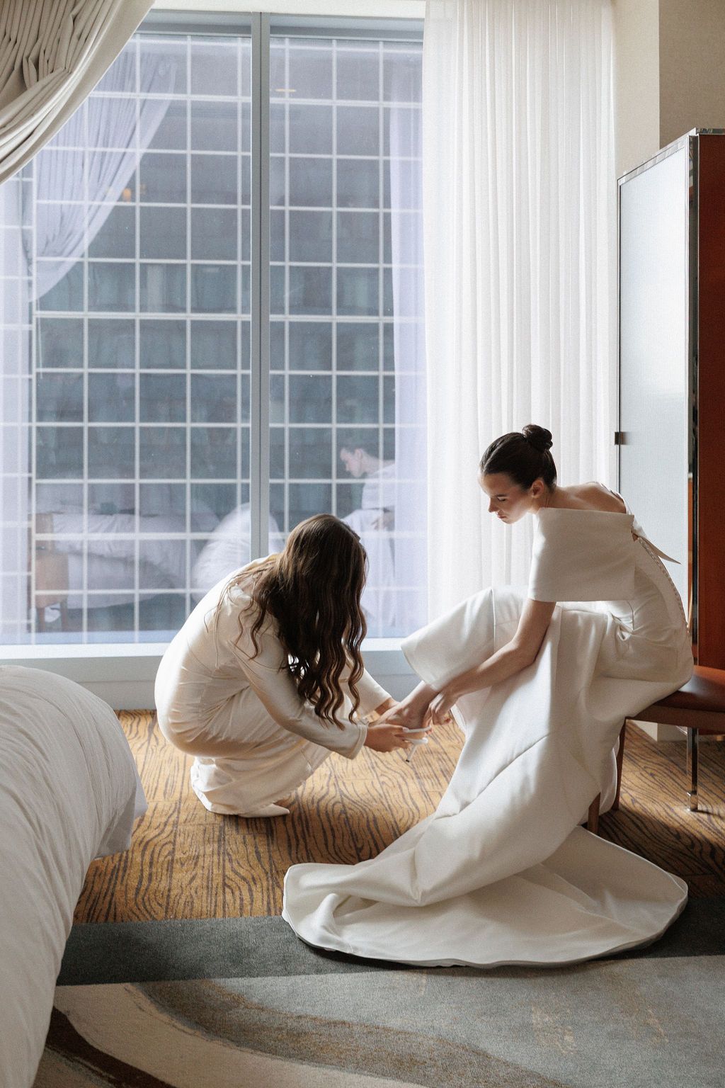 Ethereal sequence of a figure in flowing white fabric moving gracefully across a sunlit hardwood floor by large windows.