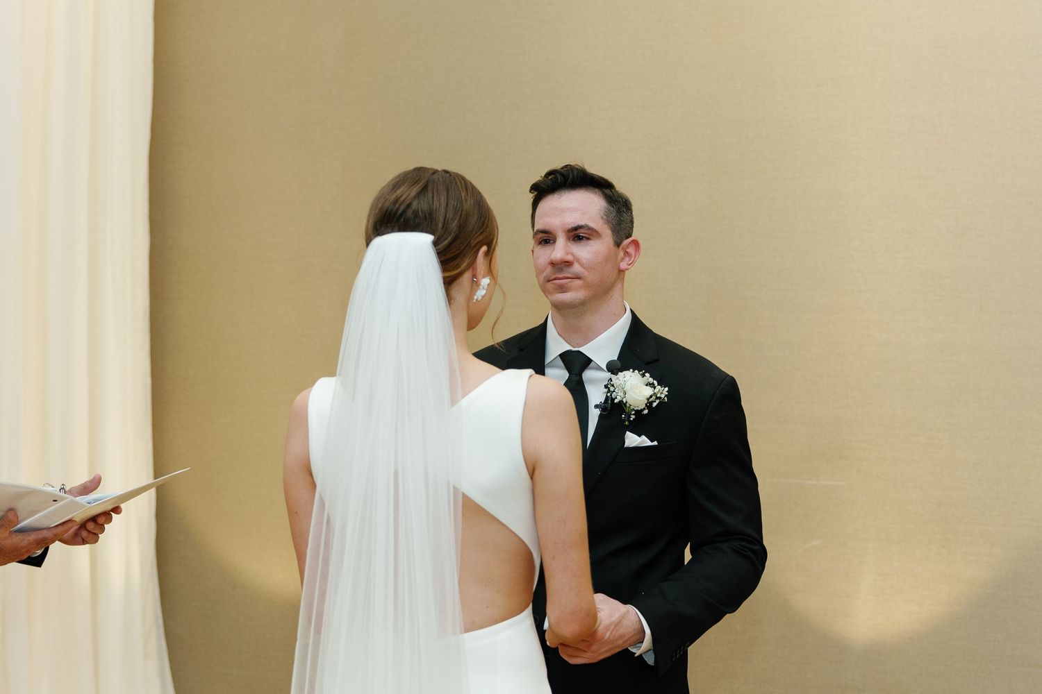 Bride and groom exchange vows during traditional wedding ceremony in elegant cream-colored venue.